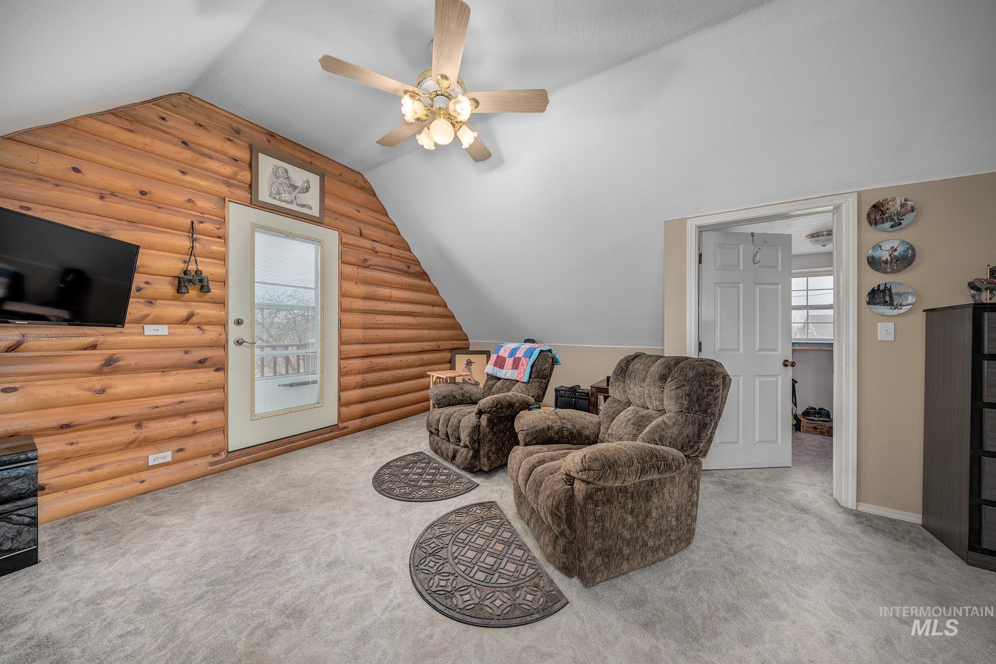 Sitting room with log walls, carpet floors, ceiling fan, vaulted ceiling, and healthy amount of natural light