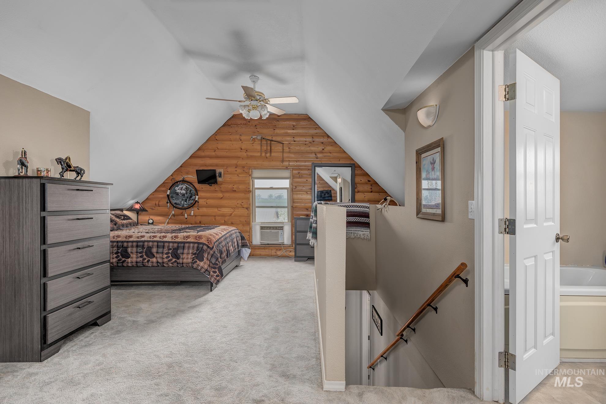 Bedroom featuring rustic walls, light carpet, vaulted ceiling, and ceiling fan