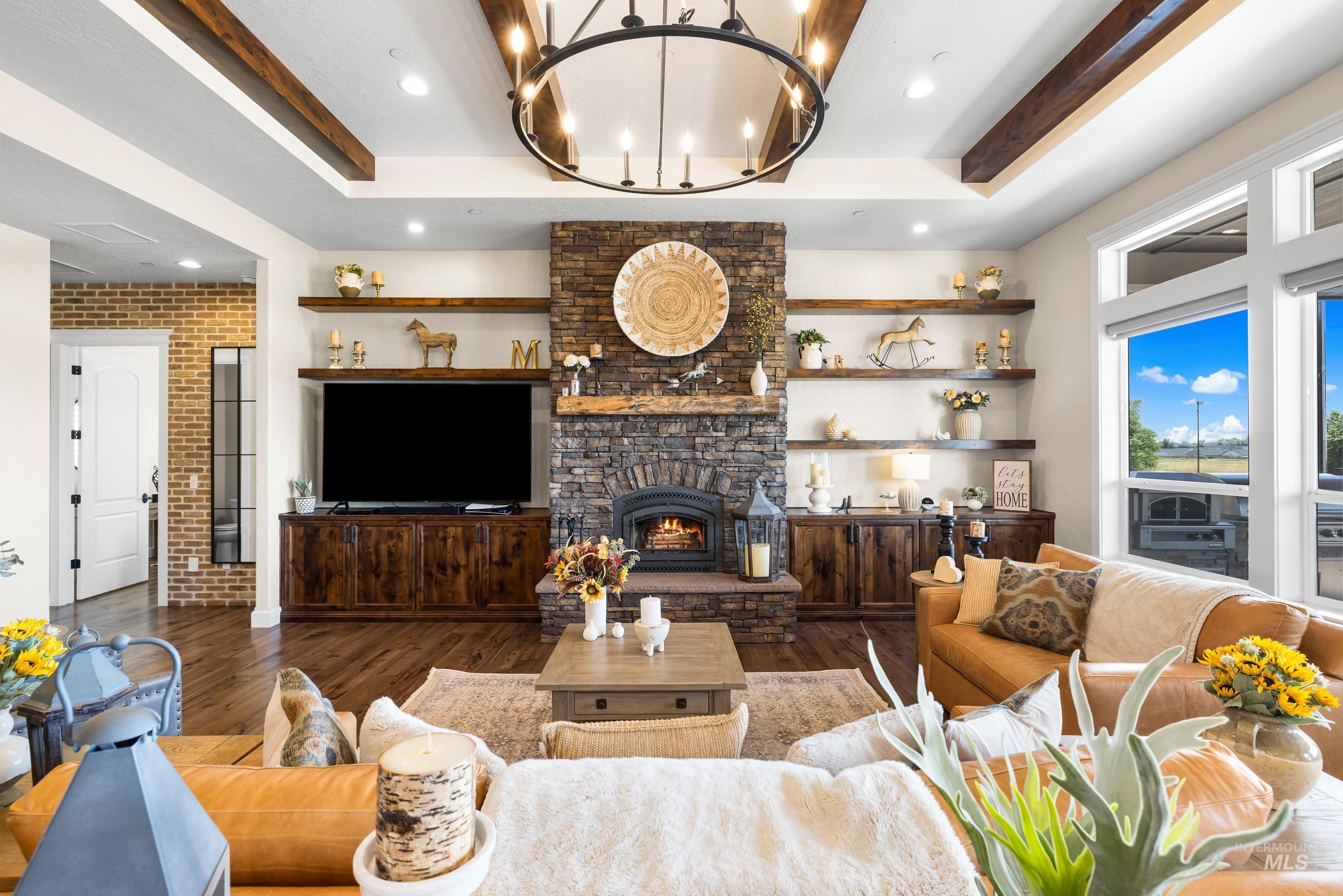 Living area featuring a raised ceiling, wood finished floors, a stone fireplace, brick wall, and recessed lighting