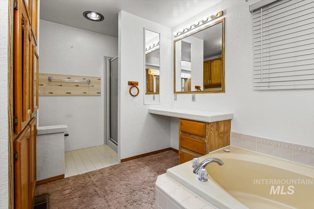 Bathroom with a garden tub, vanity, a shower stall, a textured wall, and light colored carpet