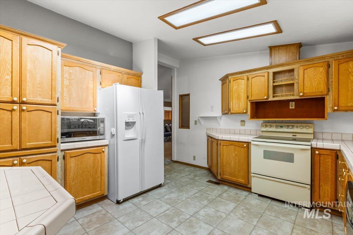 Kitchen featuring tile counters, white appliances, and brown cabinetry