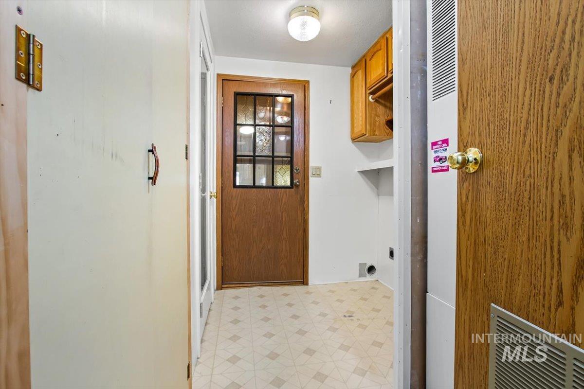 Washroom with light flooring, a heating unit, hookup for an electric dryer, and cabinet space