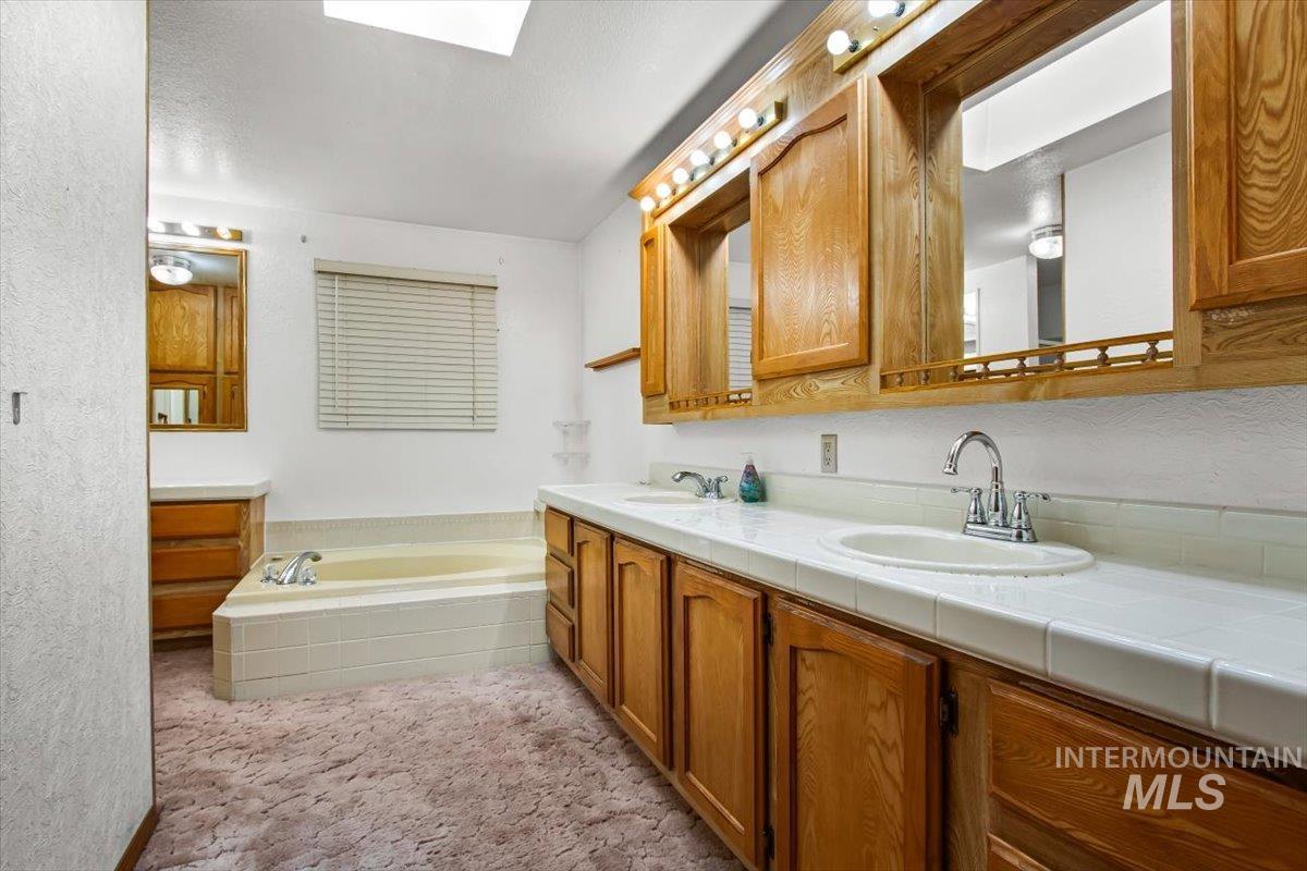 Bathroom featuring double vanity, a garden tub, light carpet, a skylight, and a textured wall