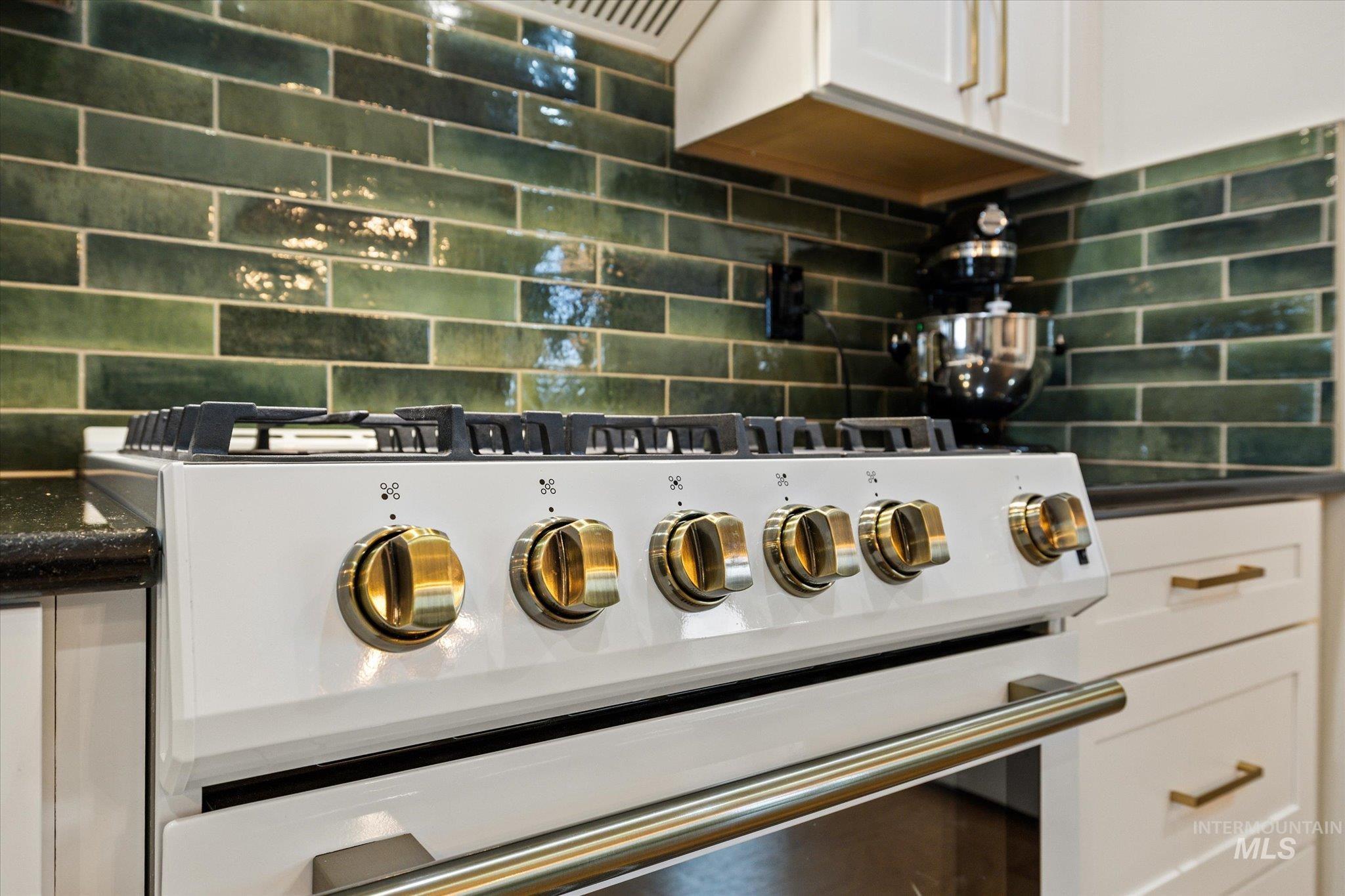 Kitchen view of white cabinets, high end range, and tasteful backsplash