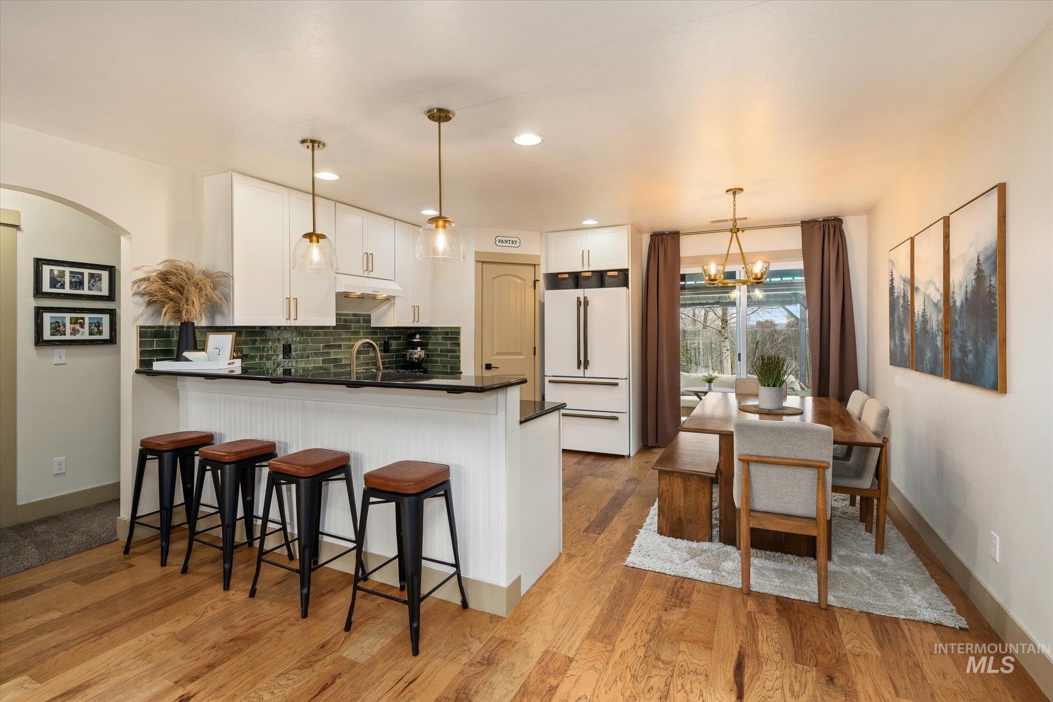 Kitchen with white cabinets, a breakfast bar area, freestanding refrigerator, suspended lighting, and a peninsula