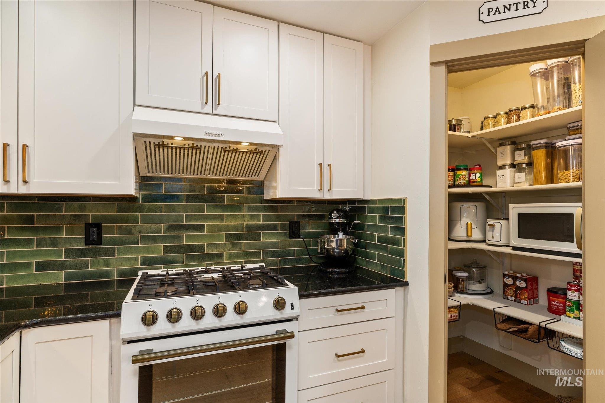 Kitchen featuring white appliances, extractor fan, and white cabinetry