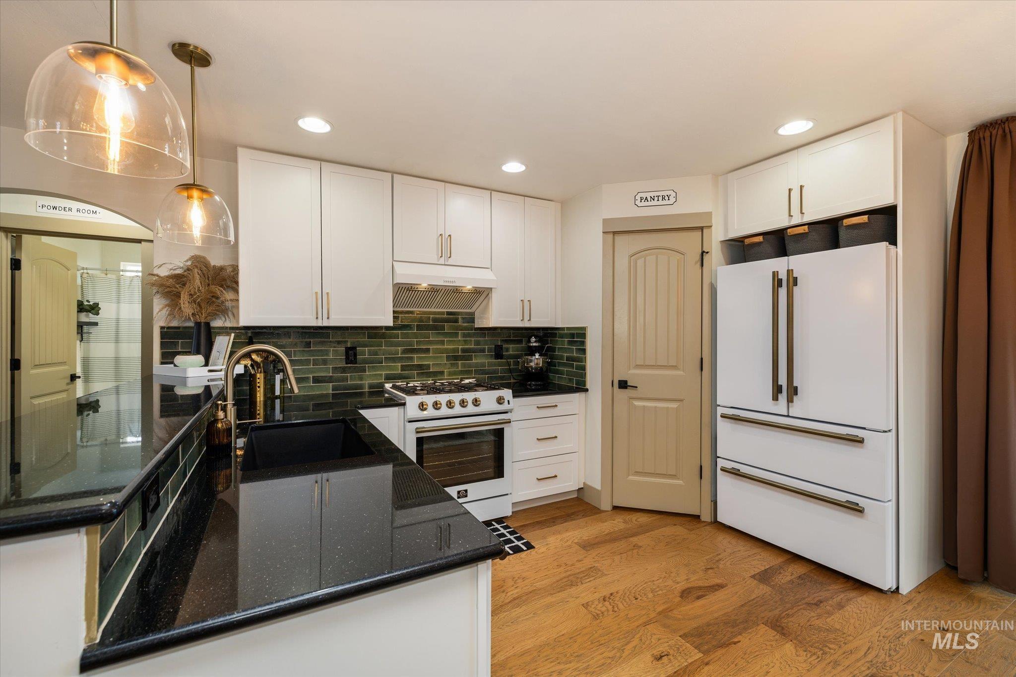Kitchen with white appliances, dark stone counters, white cabinets, and light wood-style floors