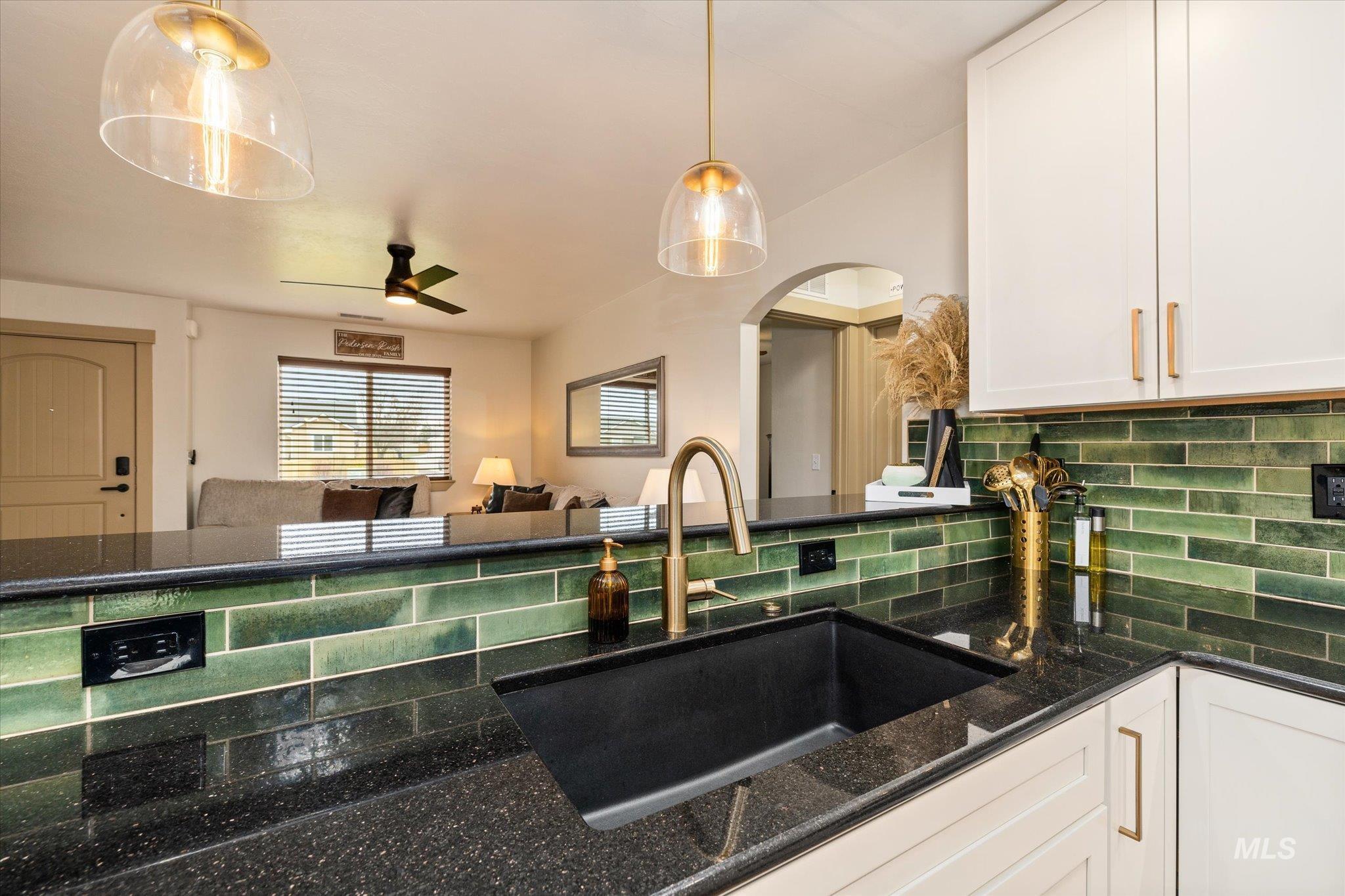 Kitchen featuring white cabinetry, dark stone countertops, ceiling fan, decorative backsplash, and hanging light fixtures