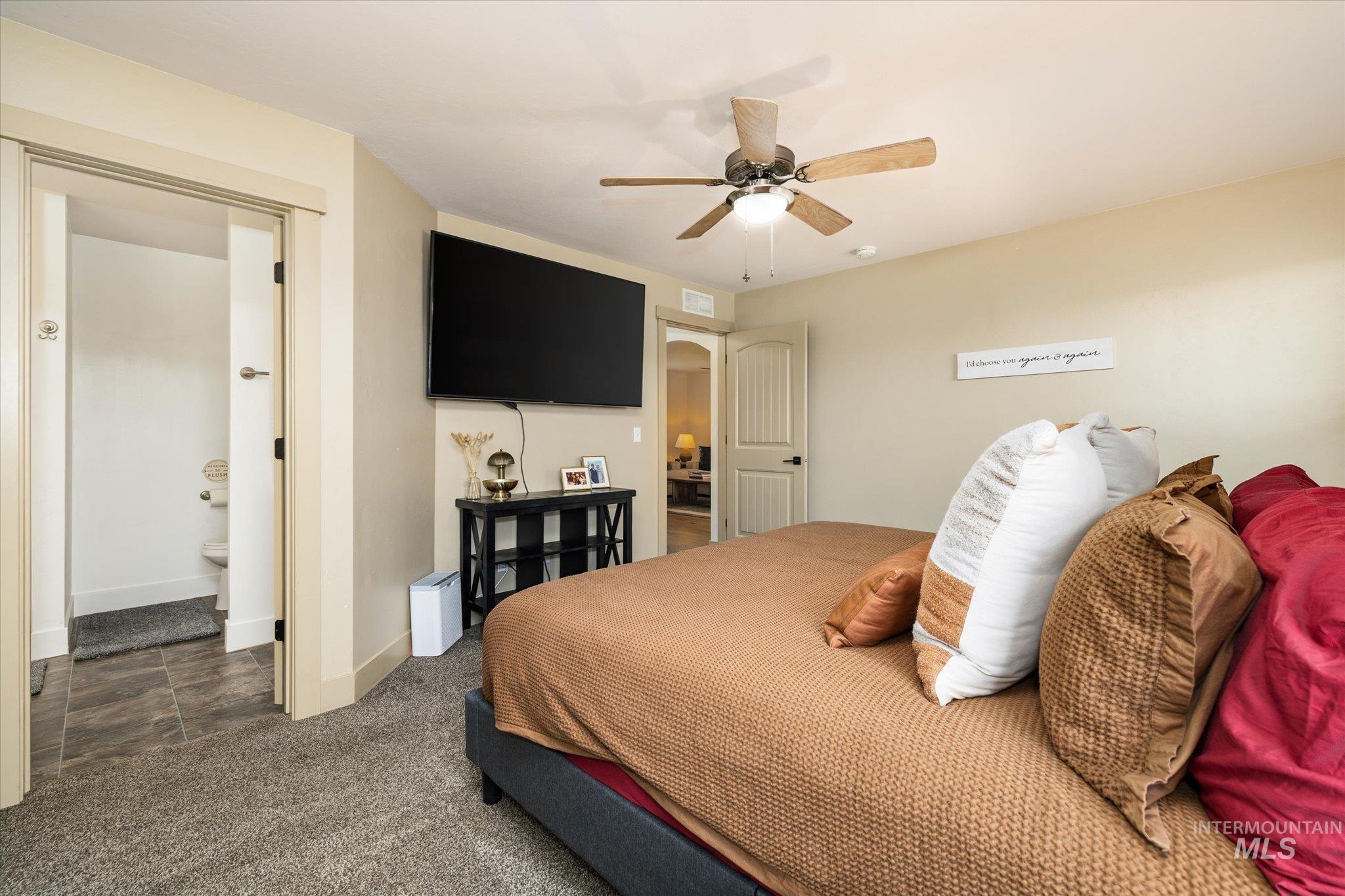 Bedroom with a ceiling fan, dark carpet, and ensuite bath
