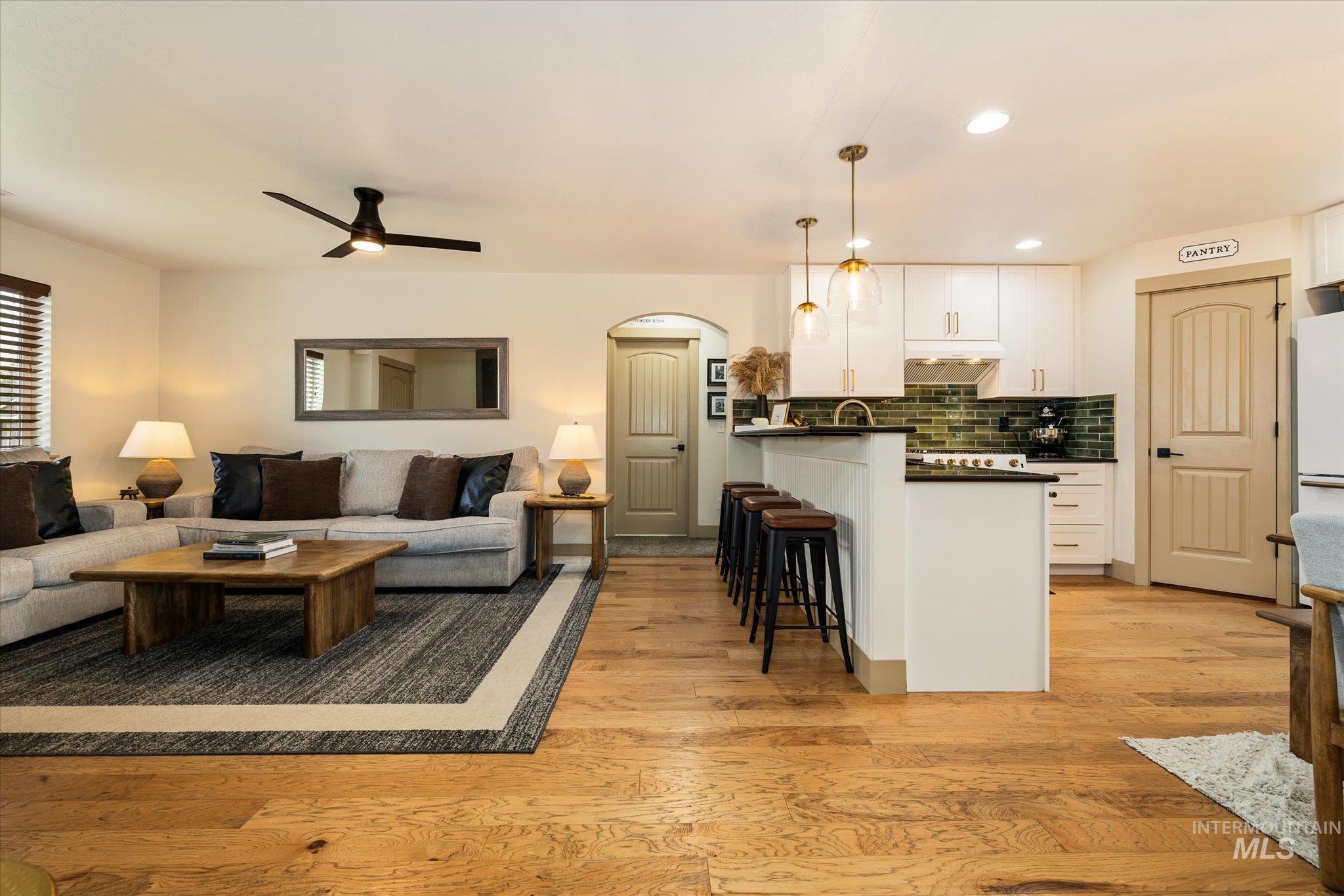 Living area featuring light wood-type flooring, ceiling fan, arched walkways, and recessed lighting