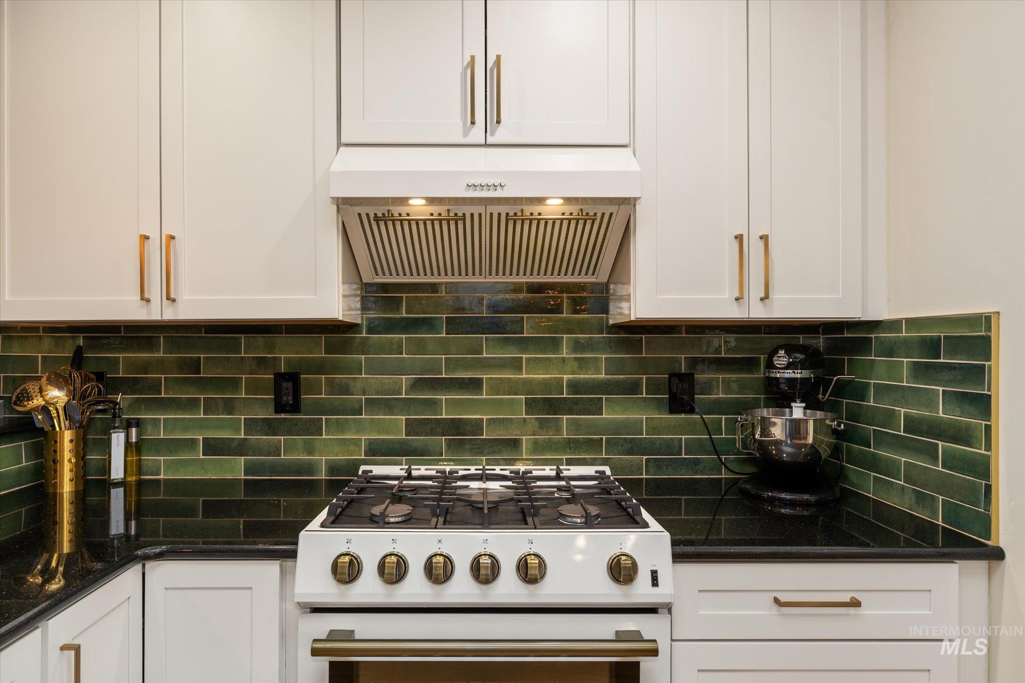 Kitchen featuring high end stove, dark stone counters, white cabinets, extractor fan, and decorative backsplash