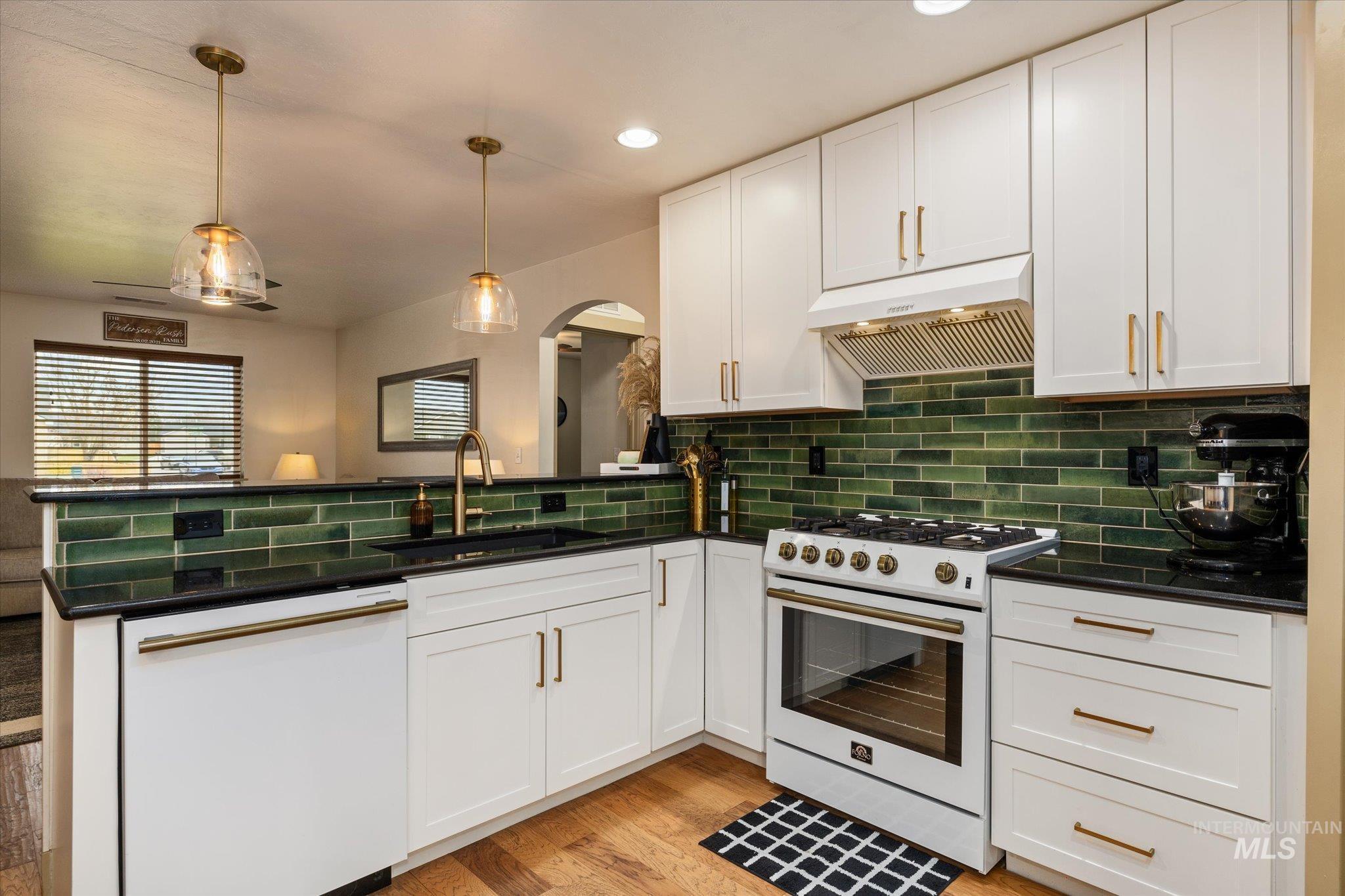 Kitchen with white appliances, white cabinetry, a peninsula, hanging light fixtures, and light wood-style flooring
