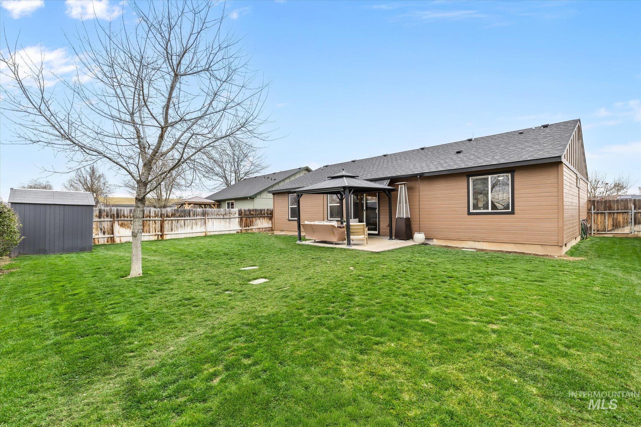 Back of house featuring a gazebo, a patio, a shed, a fenced backyard, and roof with shingles