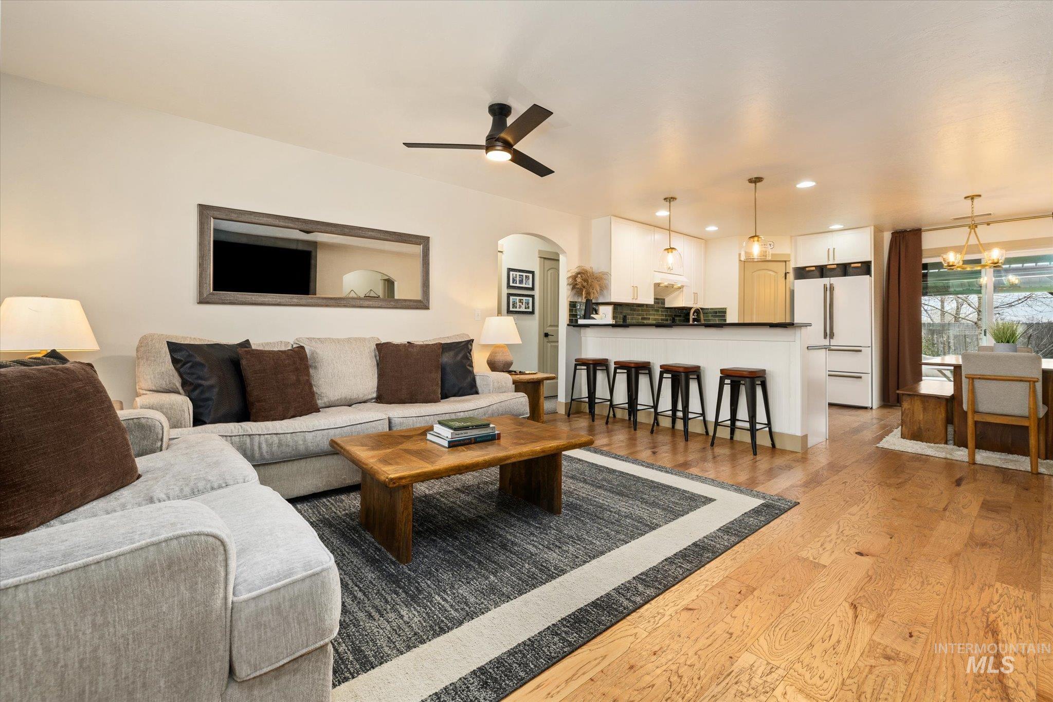 Living area with arched walkways, light wood finished floors, ceiling fan, and recessed lighting