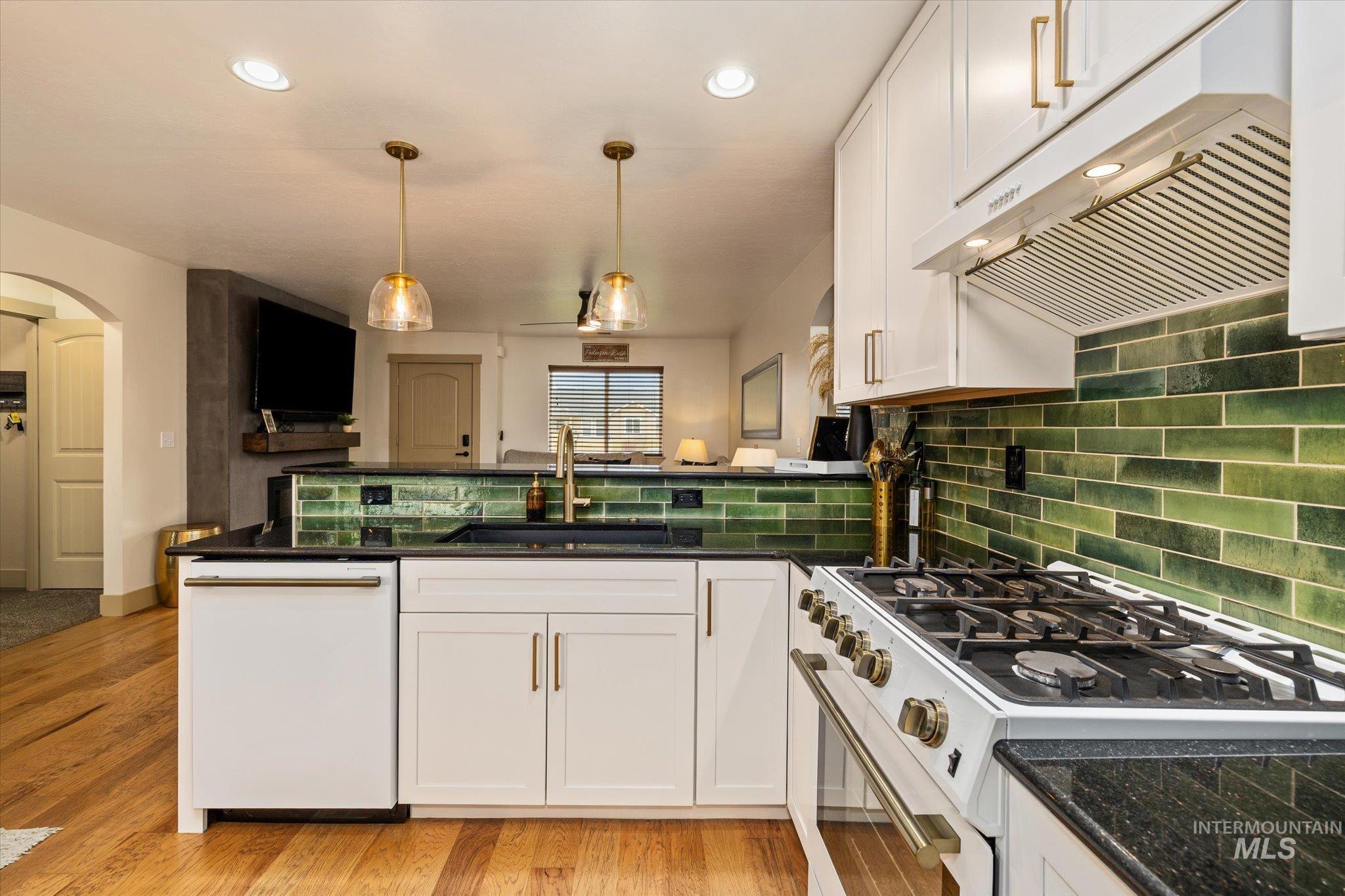 Kitchen featuring white appliances, white cabinetry, pendant lighting, arched walkways, and a peninsula