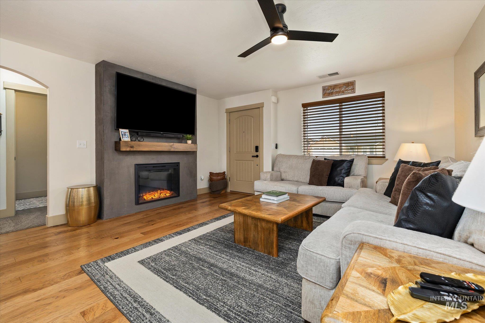 Living area featuring wood finished floors, a ceiling fan, a large fireplace, and arched walkways