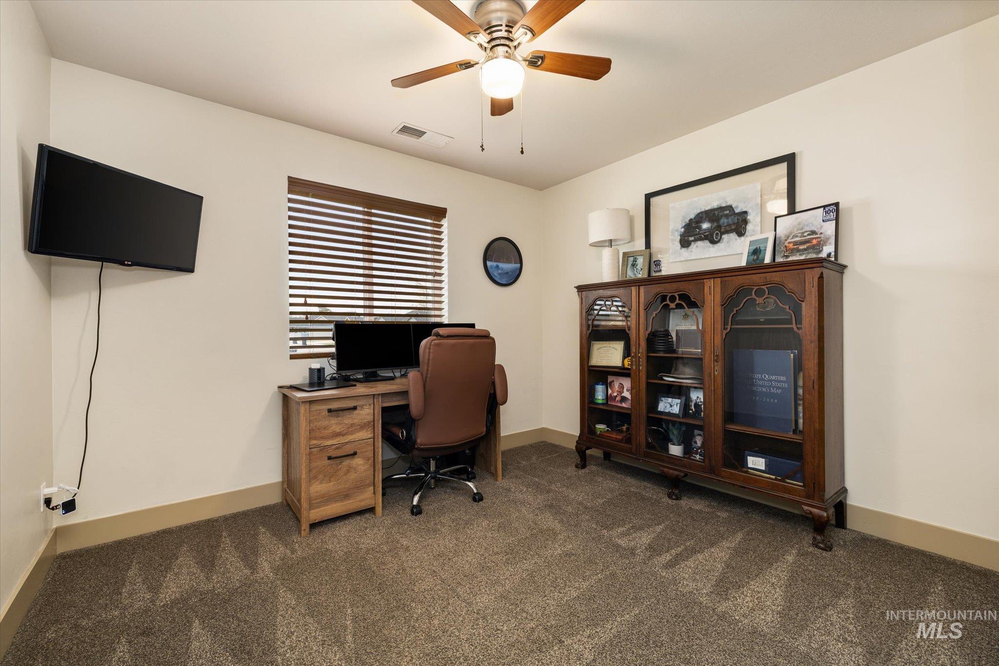 Office area featuring a ceiling fan and dark carpet