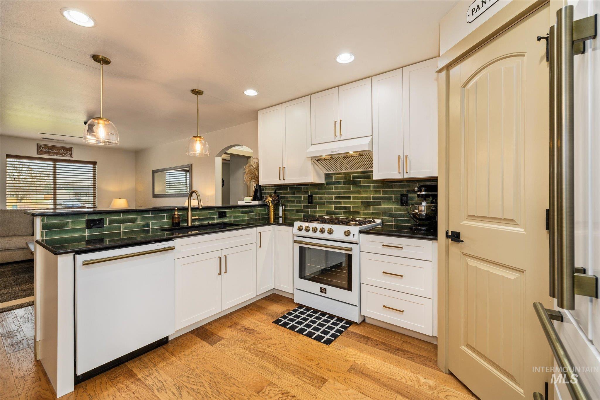 Kitchen with a peninsula, gas range oven, dishwasher, light wood-style floors, and white cabinets