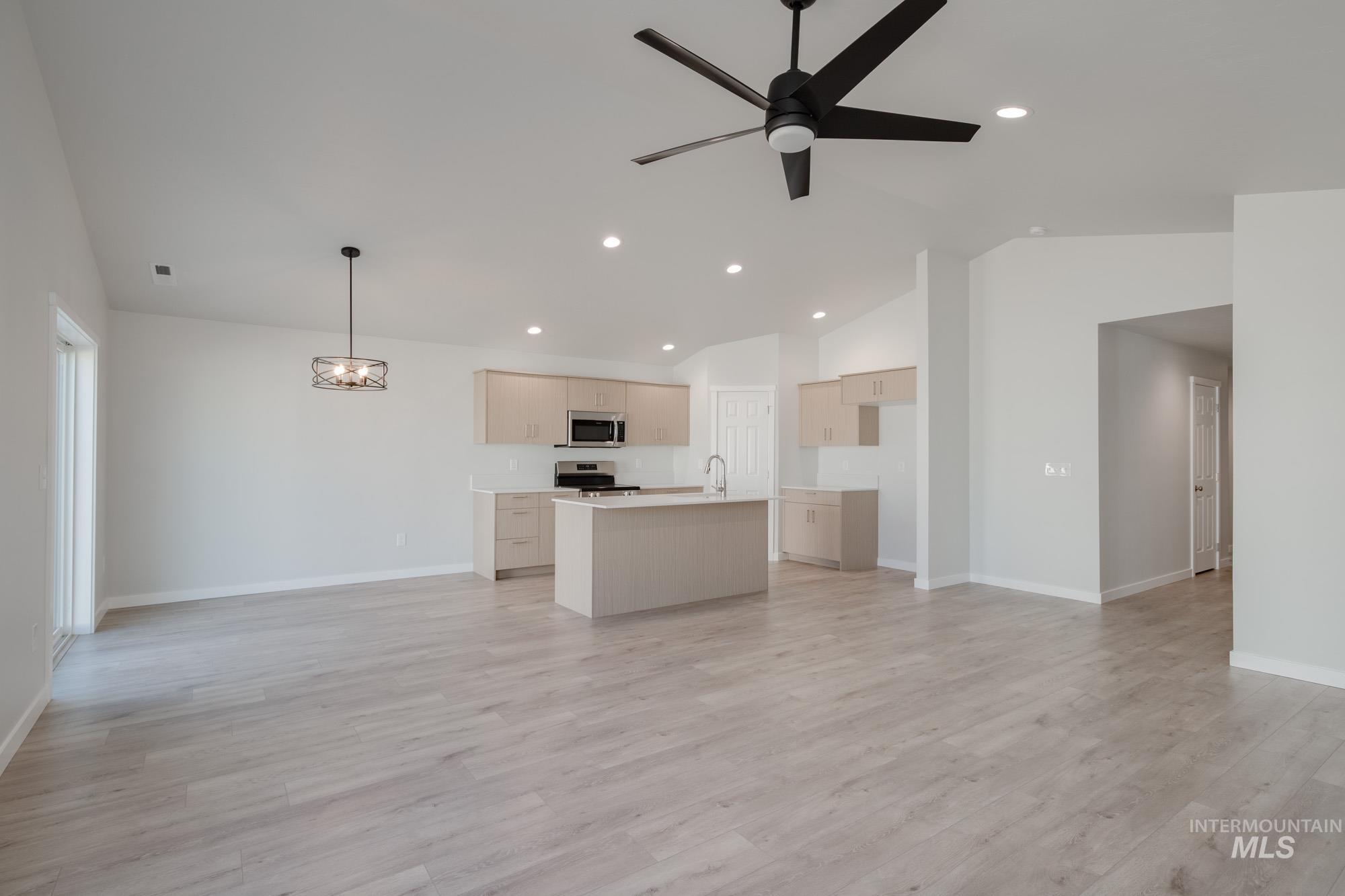 Unfurnished living room featuring vaulted ceiling, light wood finished floors, recessed lighting, ceiling fan, and a chandelier