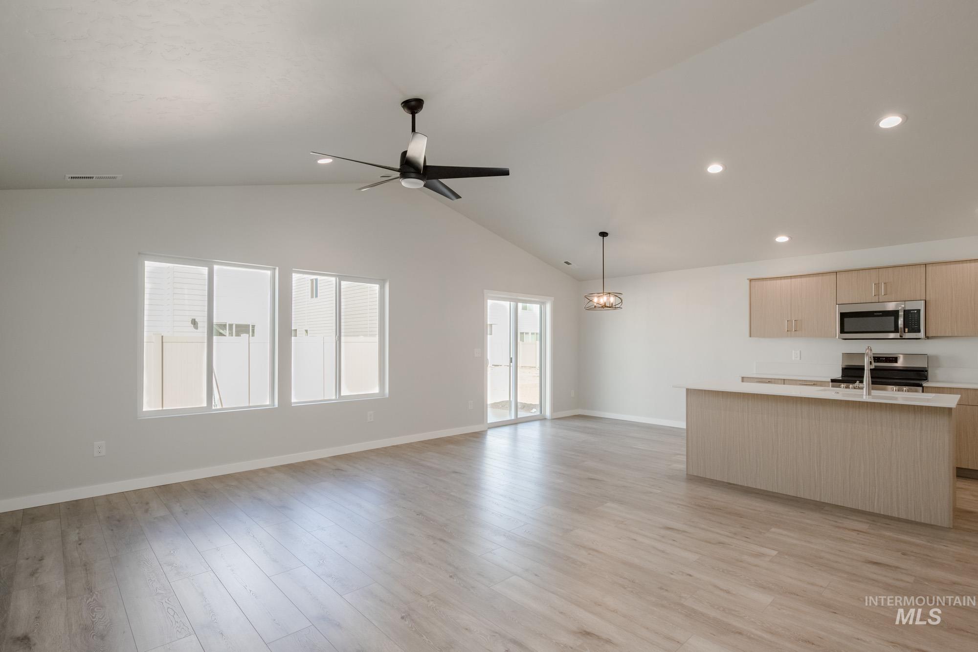 Kitchen featuring open floor plan, light countertops, an island with sink, light brown cabinetry, and lofted ceiling