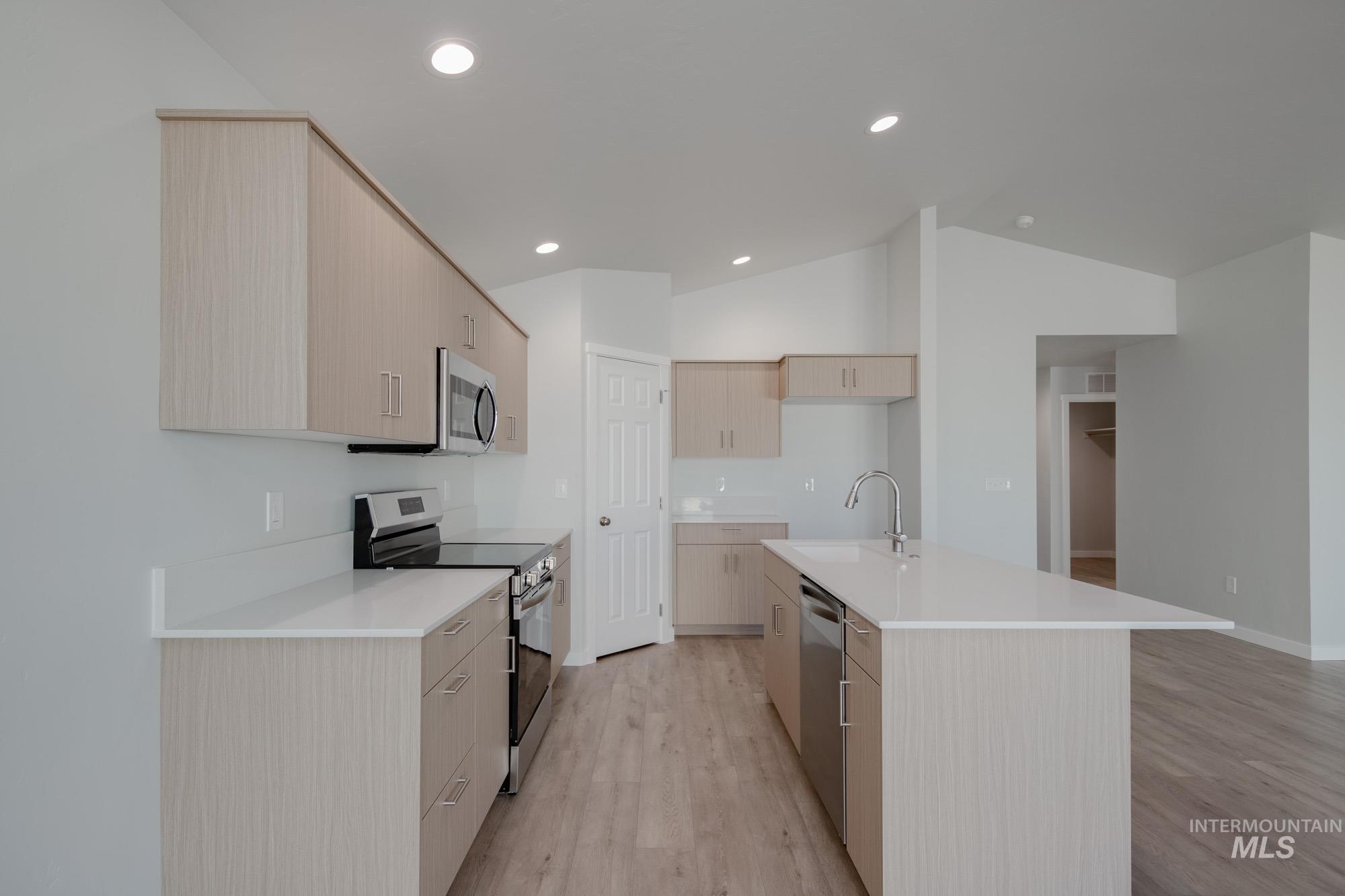 Kitchen with appliances with stainless steel finishes, light wood-style floors, light brown cabinetry, modern cabinets, and lofted ceiling
