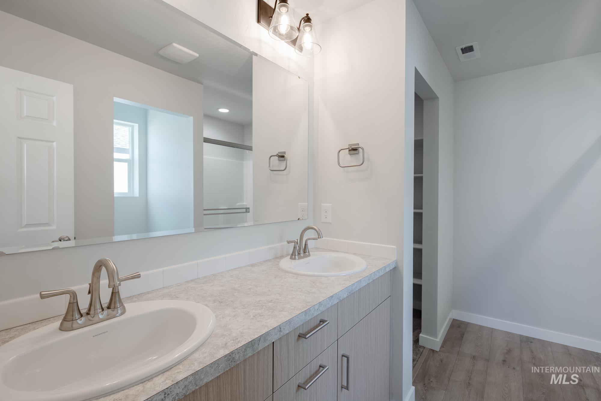 Bathroom with light wood-style floors, a shower with door, and double vanity