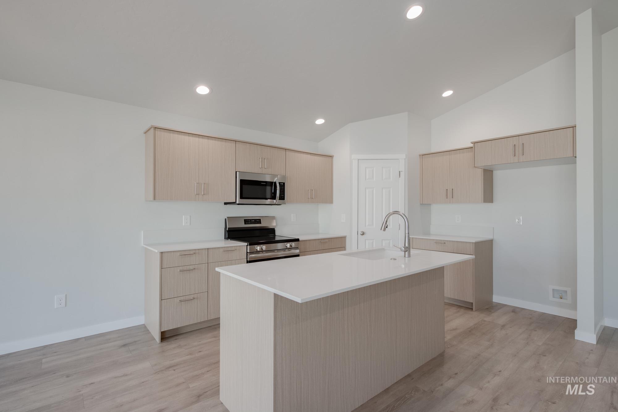Kitchen with light brown cabinetry, stainless steel appliances, light wood-style flooring, recessed lighting, and lofted ceiling