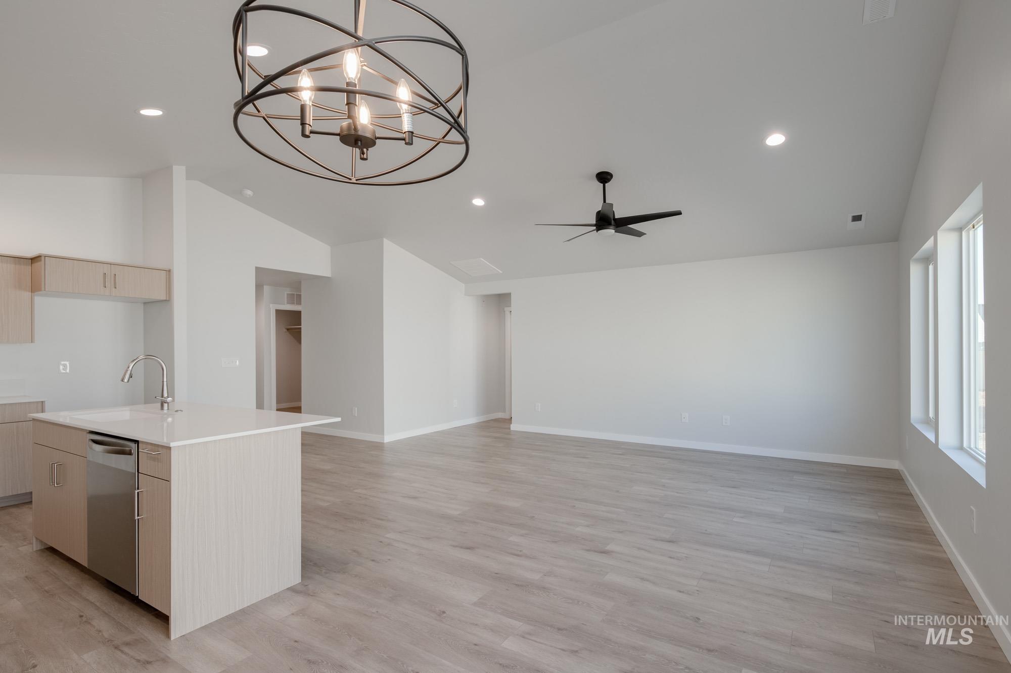 Kitchen with vaulted ceiling, light wood finished floors, a kitchen island with sink, stainless steel dishwasher, and a chandelier