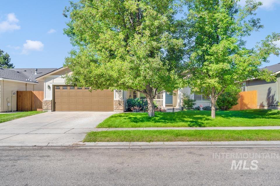 View of property hidden behind natural elements with concrete driveway, a garage, and stone siding