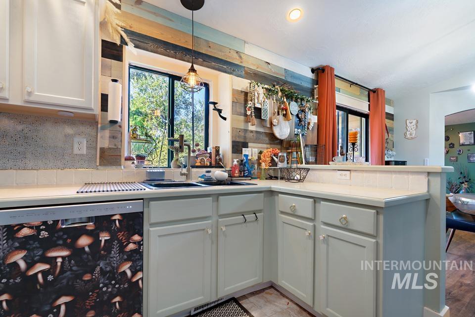 Kitchen with light countertops, stainless steel dishwasher, a peninsula, decorative light fixtures, and white cabinets