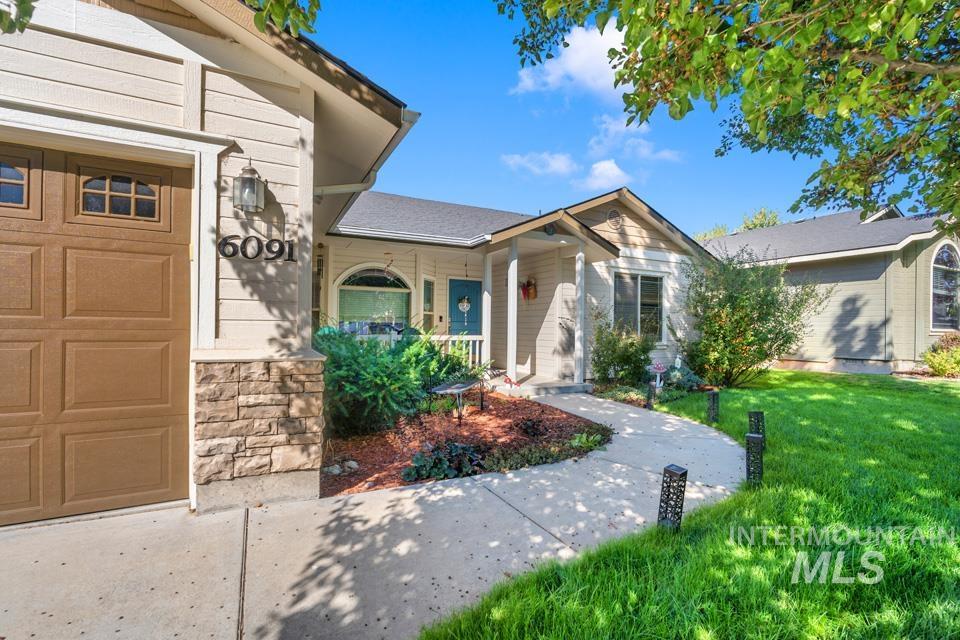 View of front of house with a porch, a front yard, a garage, and stone siding