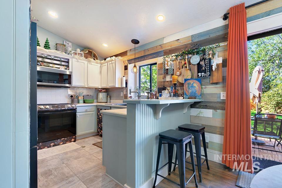 Kitchen with a breakfast bar, electric range oven, decorative light fixtures, light countertops, and decorative backsplash