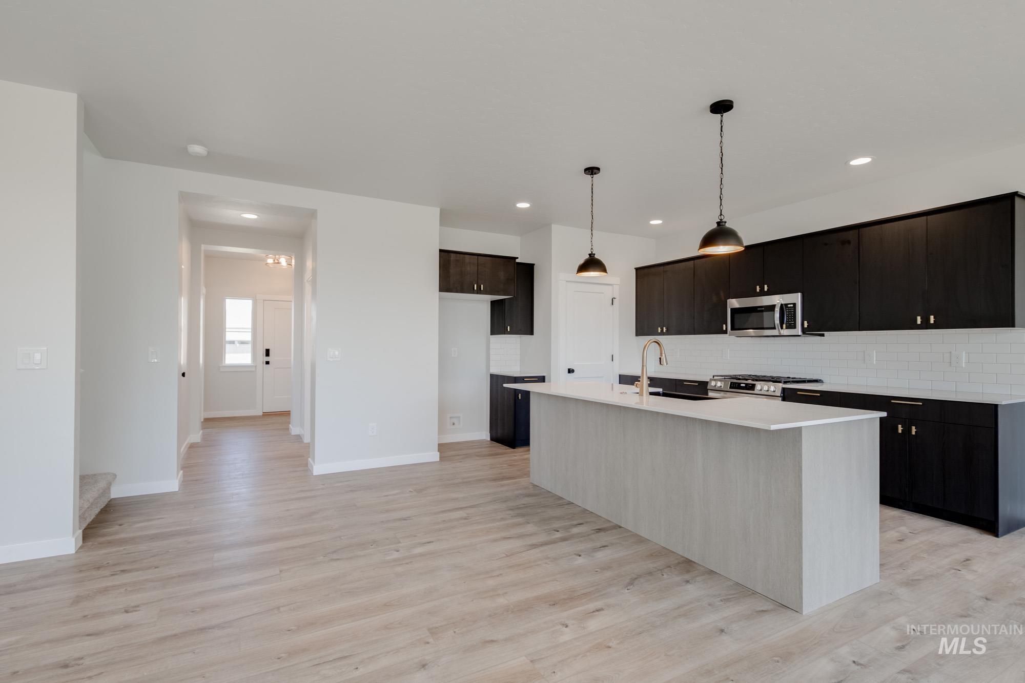 Kitchen featuring stainless steel appliances, tasteful backsplash, recessed lighting, a center island with sink, and light countertops