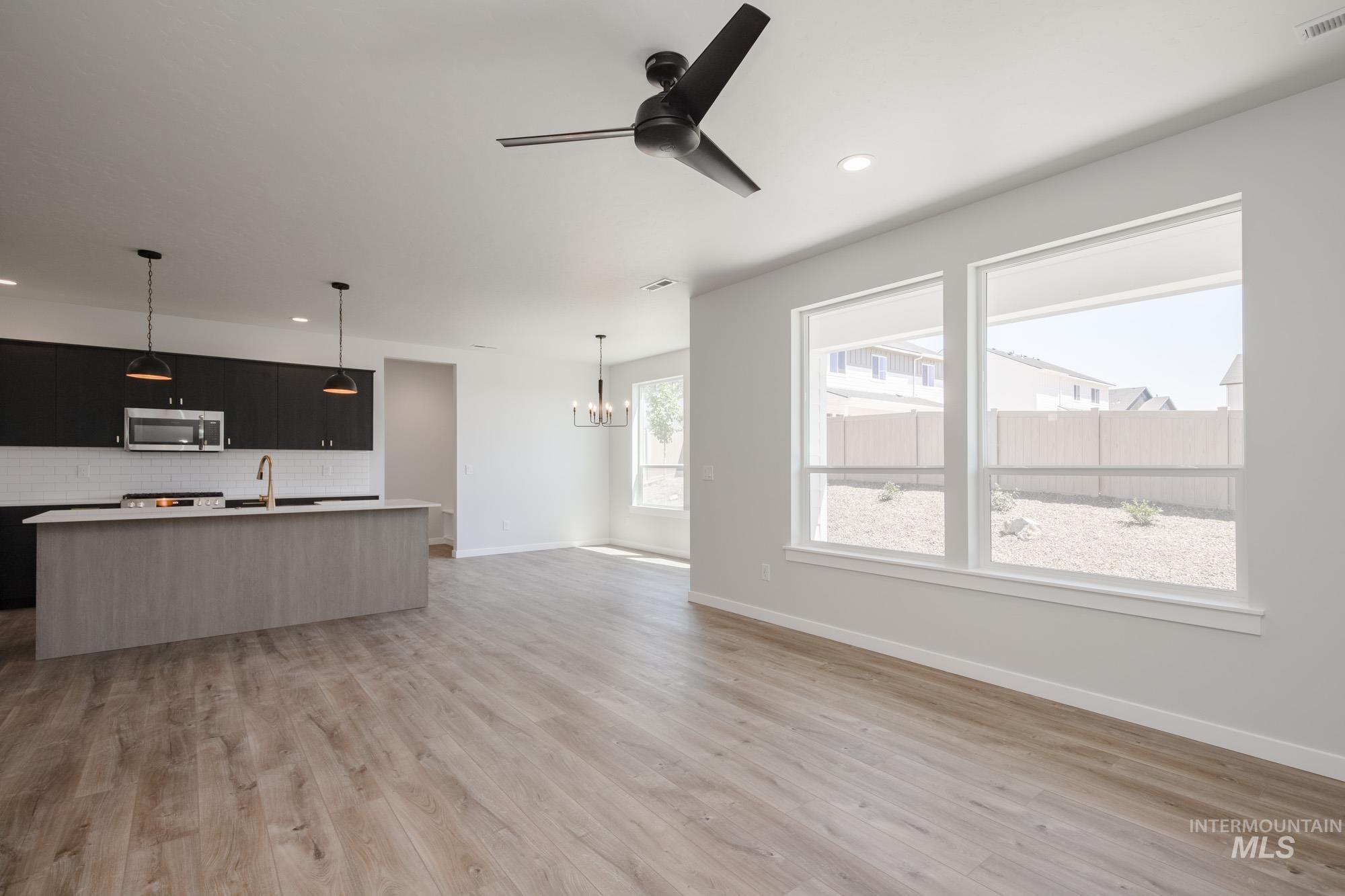 Kitchen featuring stainless steel microwave, dark cabinets, open floor plan, decorative backsplash, and a center island with sink