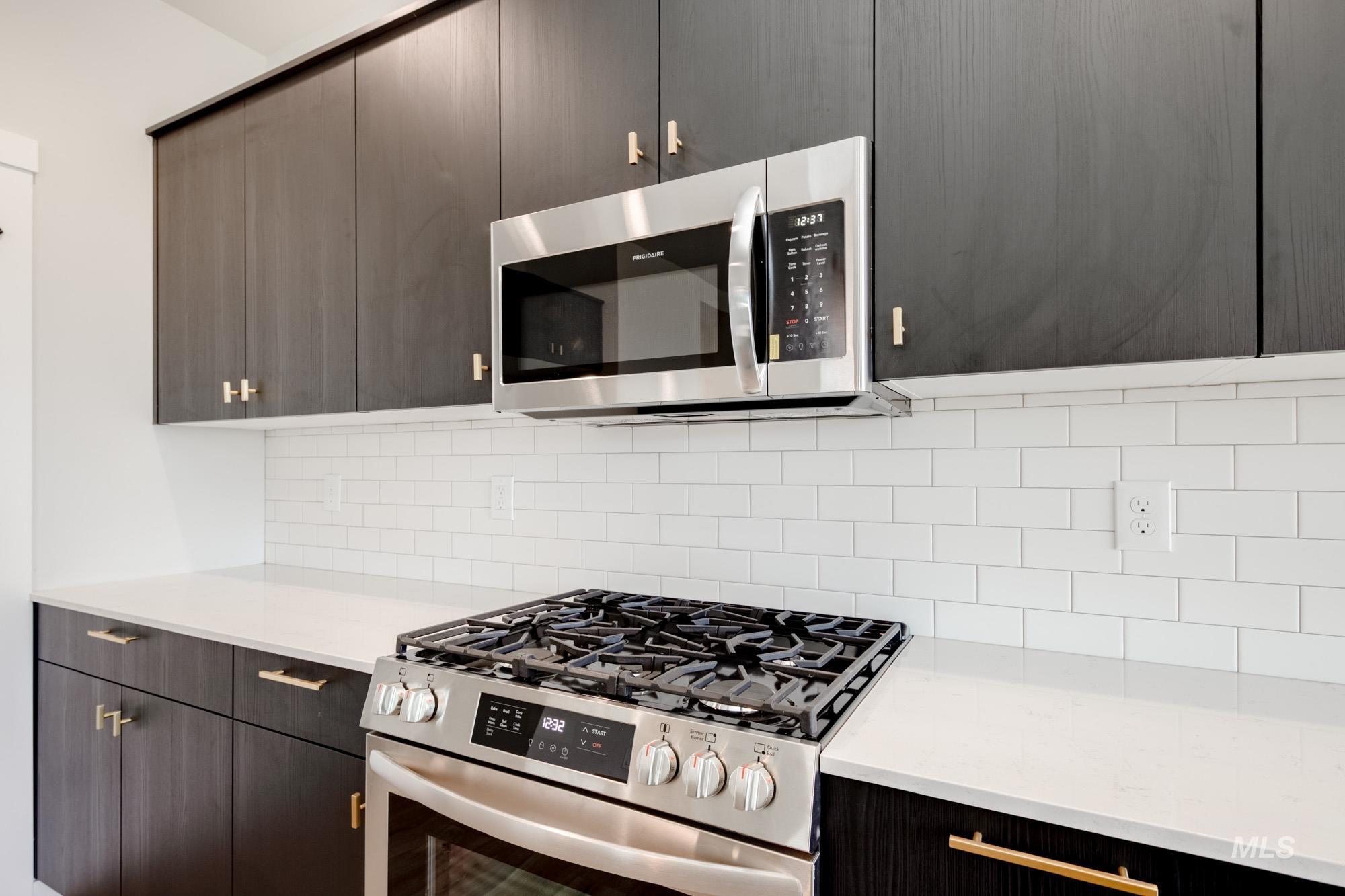 Kitchen featuring stainless steel appliances, light countertops, decorative backsplash, and dark brown cabinetry