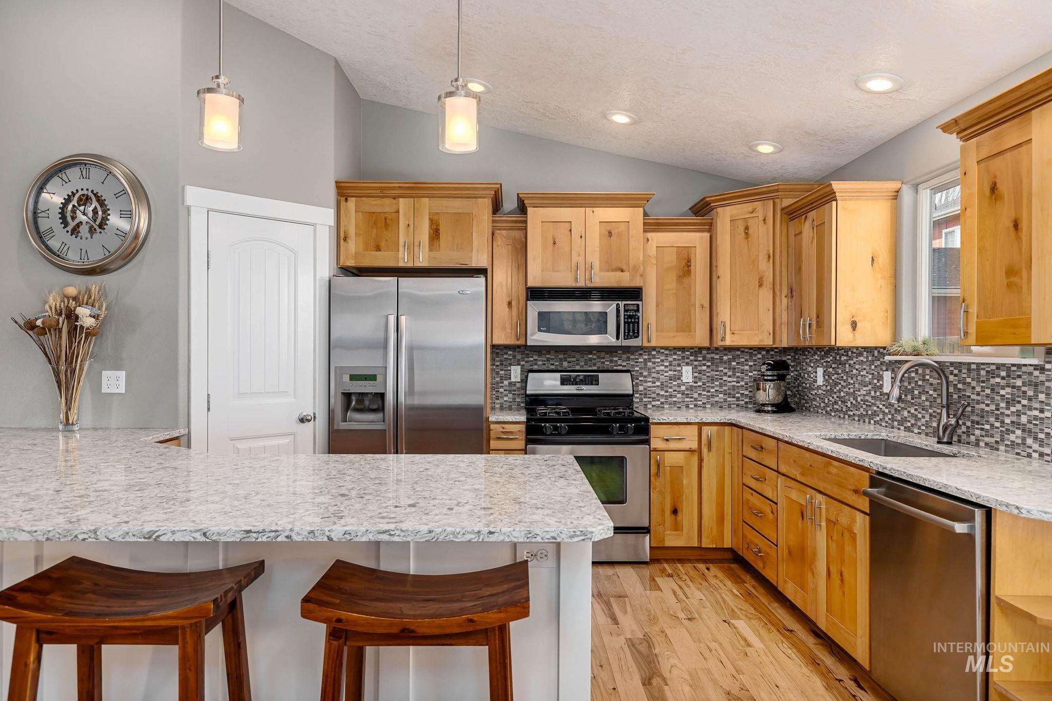 Kitchen featuring stainless steel appliances, lofted ceiling, a kitchen bar, light stone counters, and light wood finished floors