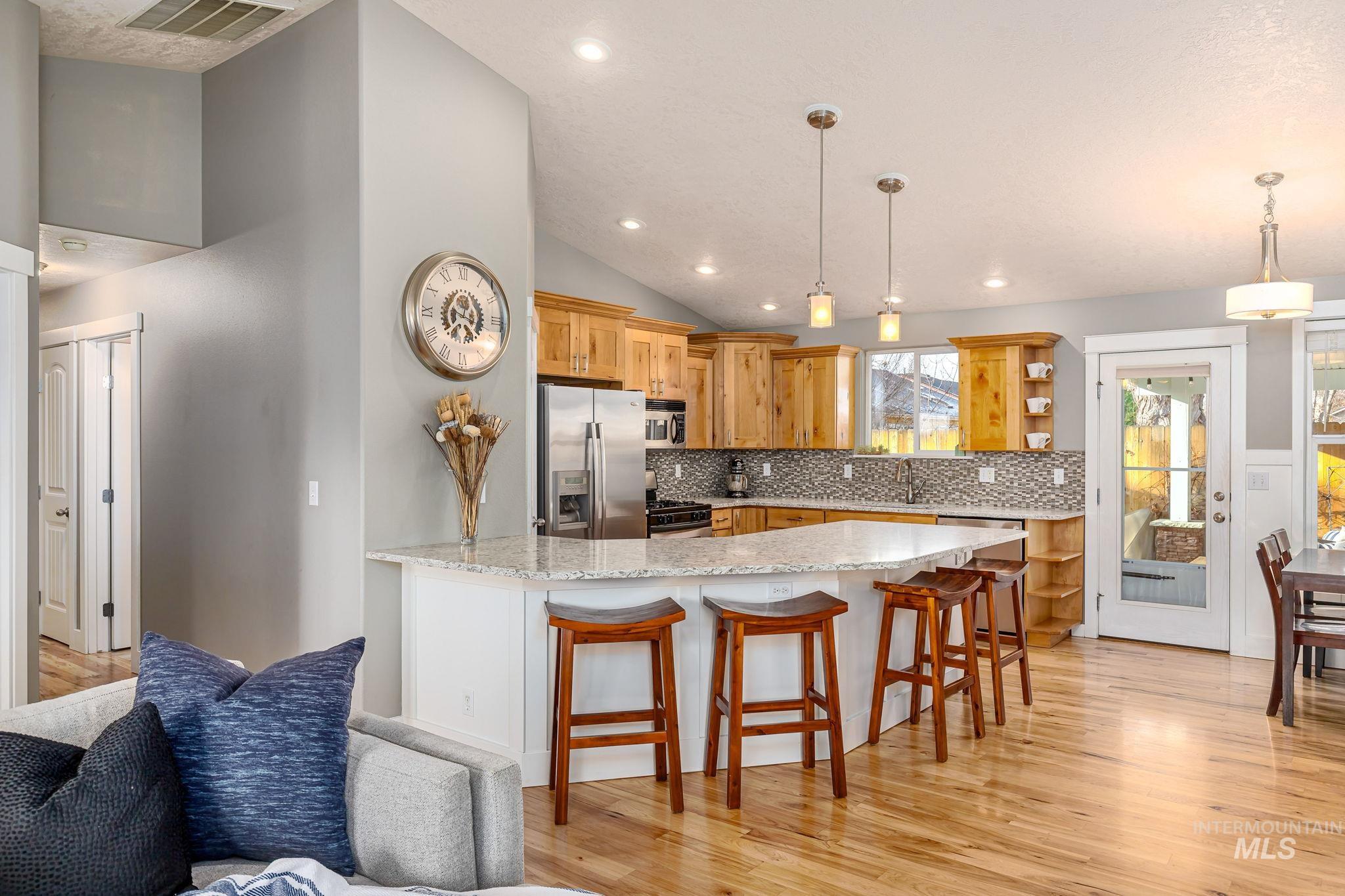 Kitchen with a breakfast bar area, a peninsula, light wood-type flooring, appliances with stainless steel finishes, and decorative light fixtures