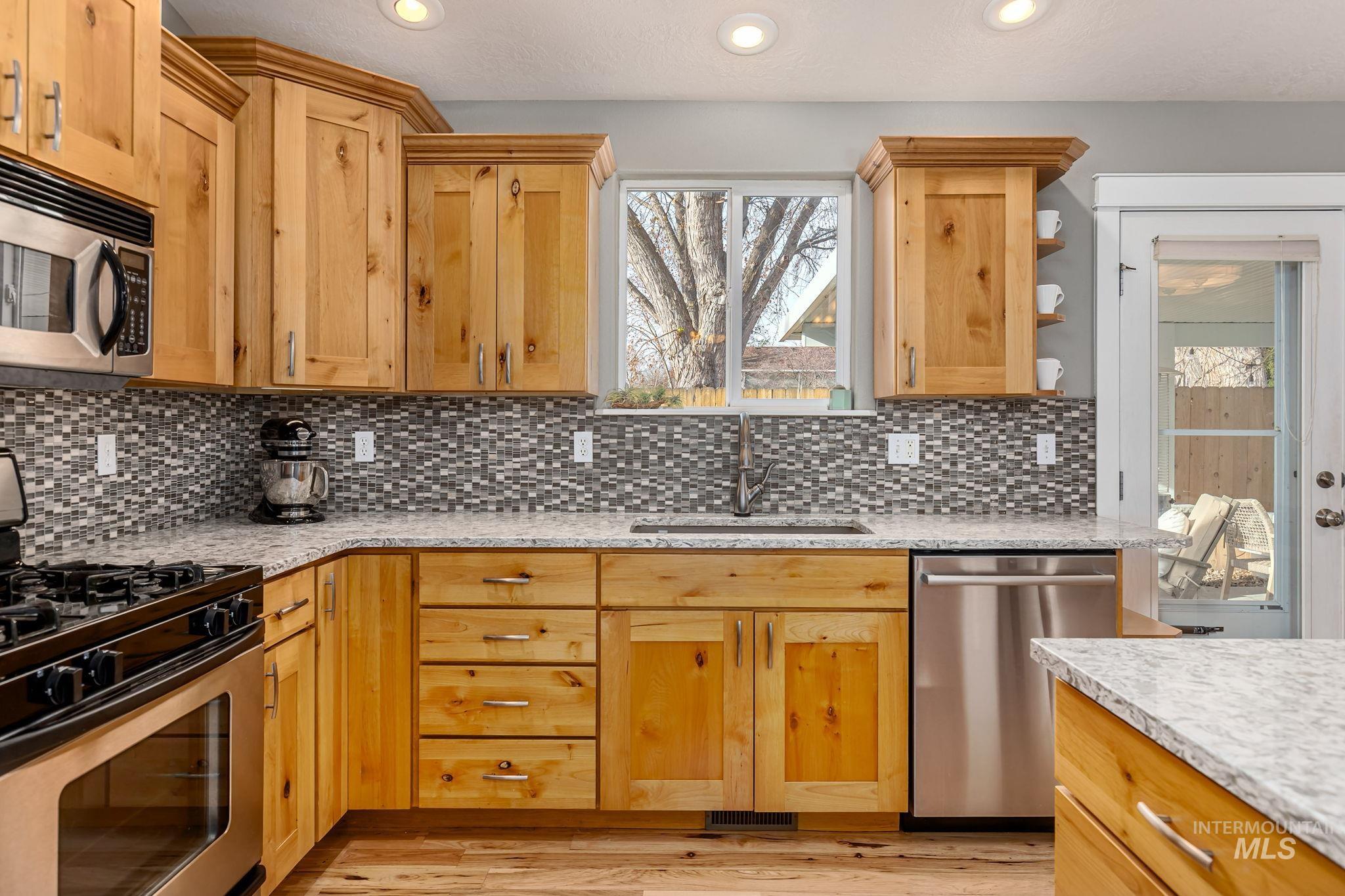 Kitchen featuring appliances with stainless steel finishes, open shelves, light stone counters, light brown cabinetry, and recessed lighting