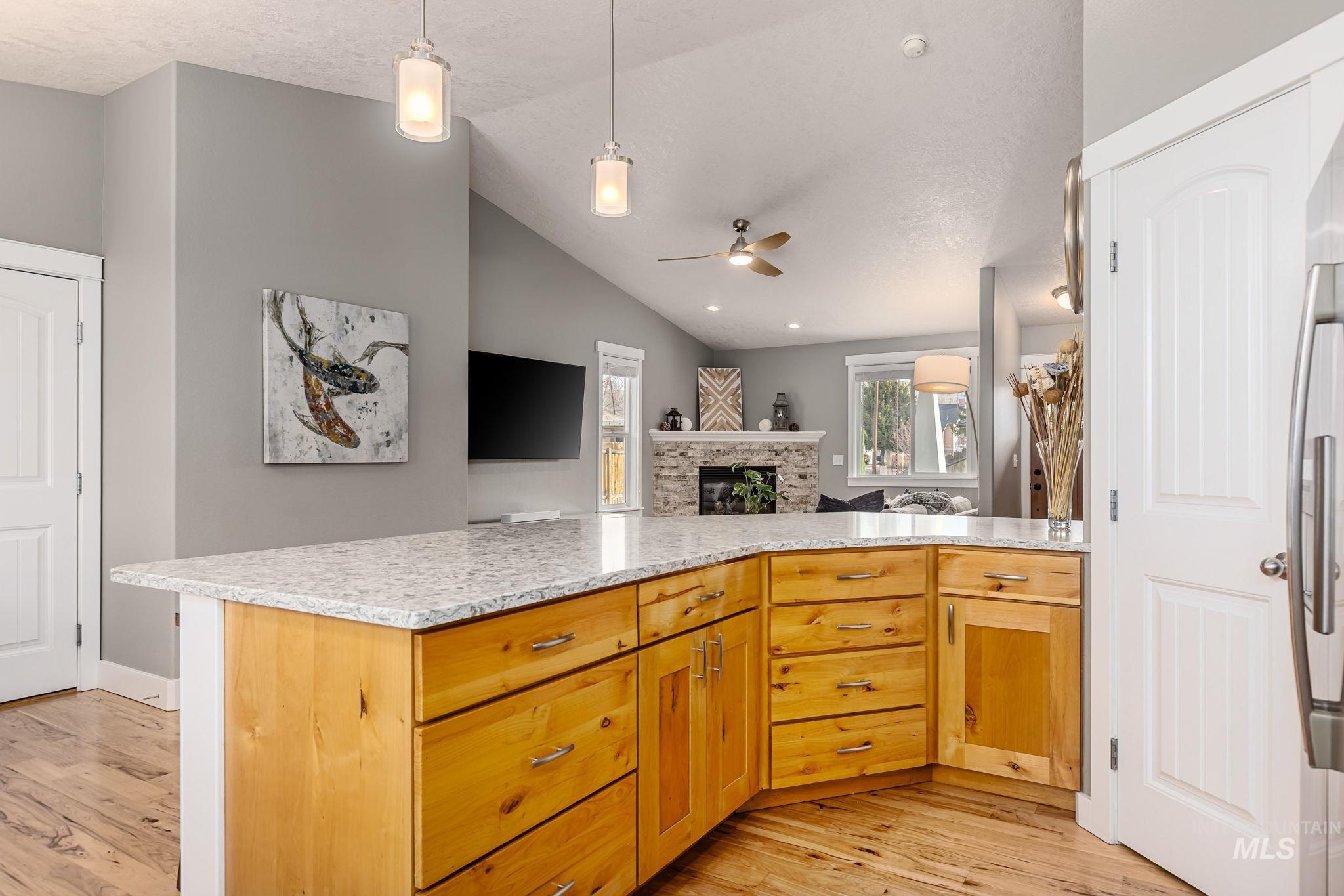 Kitchen with pendant lighting, vaulted ceiling, open floor plan, ceiling fan, and light wood-style flooring