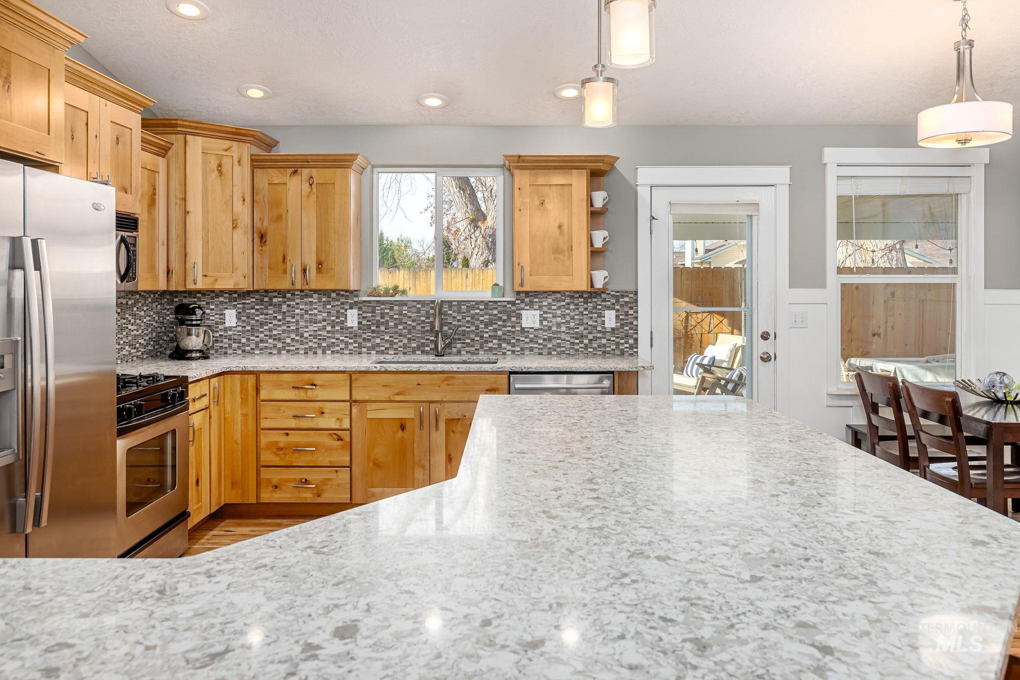Kitchen with stainless steel appliances, light stone counters, open shelves, recessed lighting, and hanging light fixtures