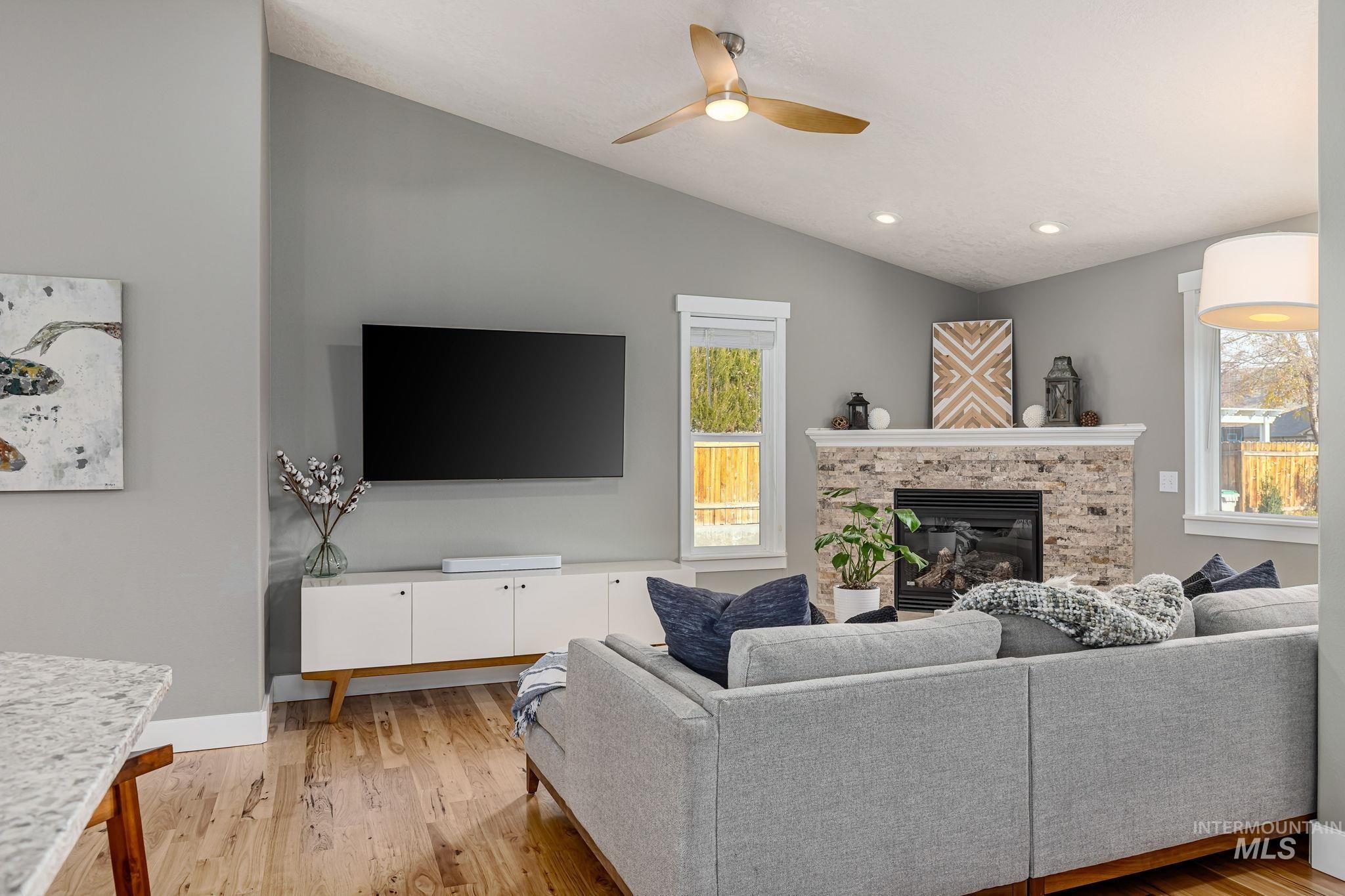 Living area featuring light wood-style floors, vaulted ceiling, a glass covered fireplace, recessed lighting, and ceiling fan