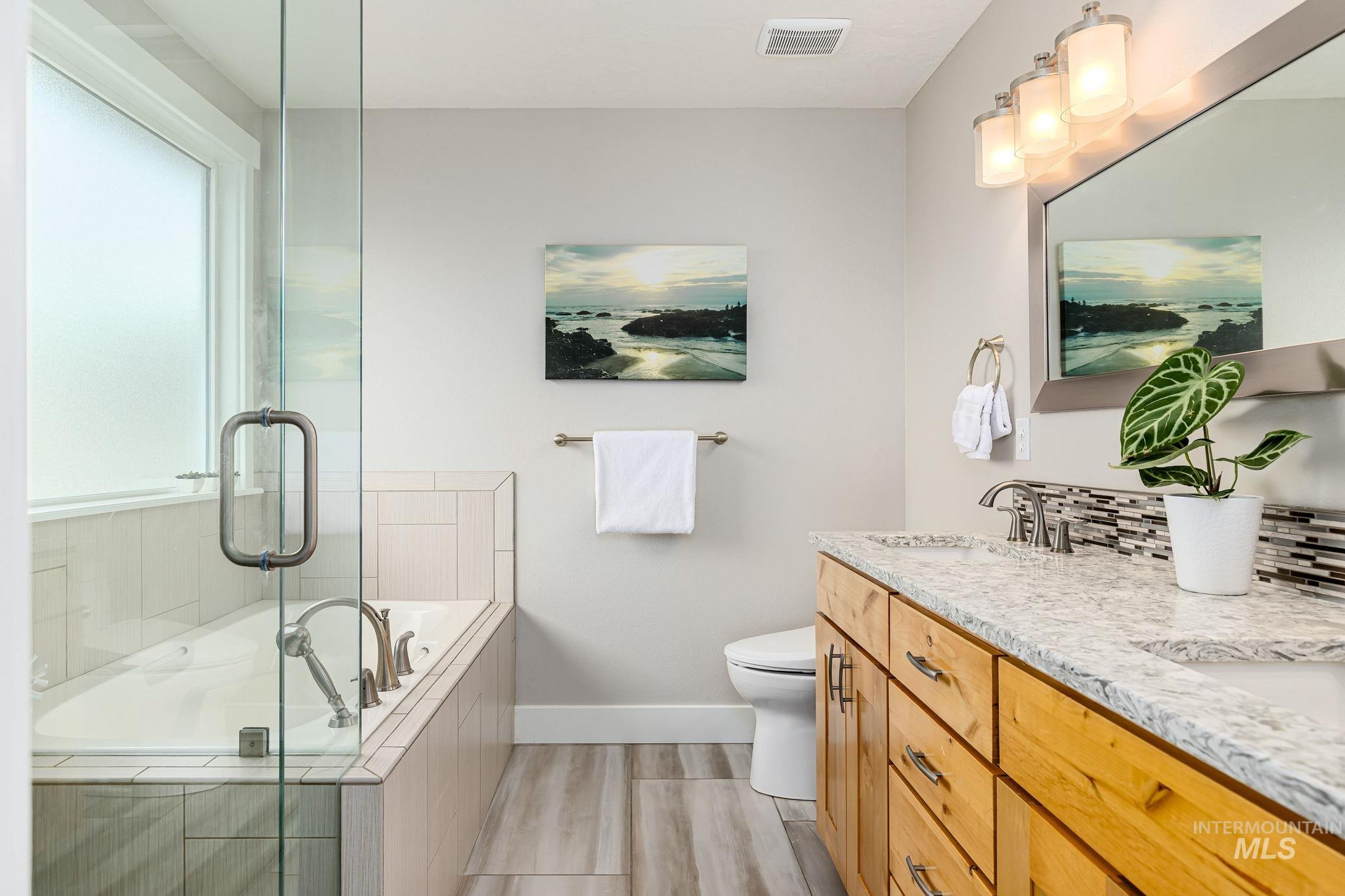 Bathroom featuring a garden tub, double vanity, a shower with door, backsplash, and light wood-style floors