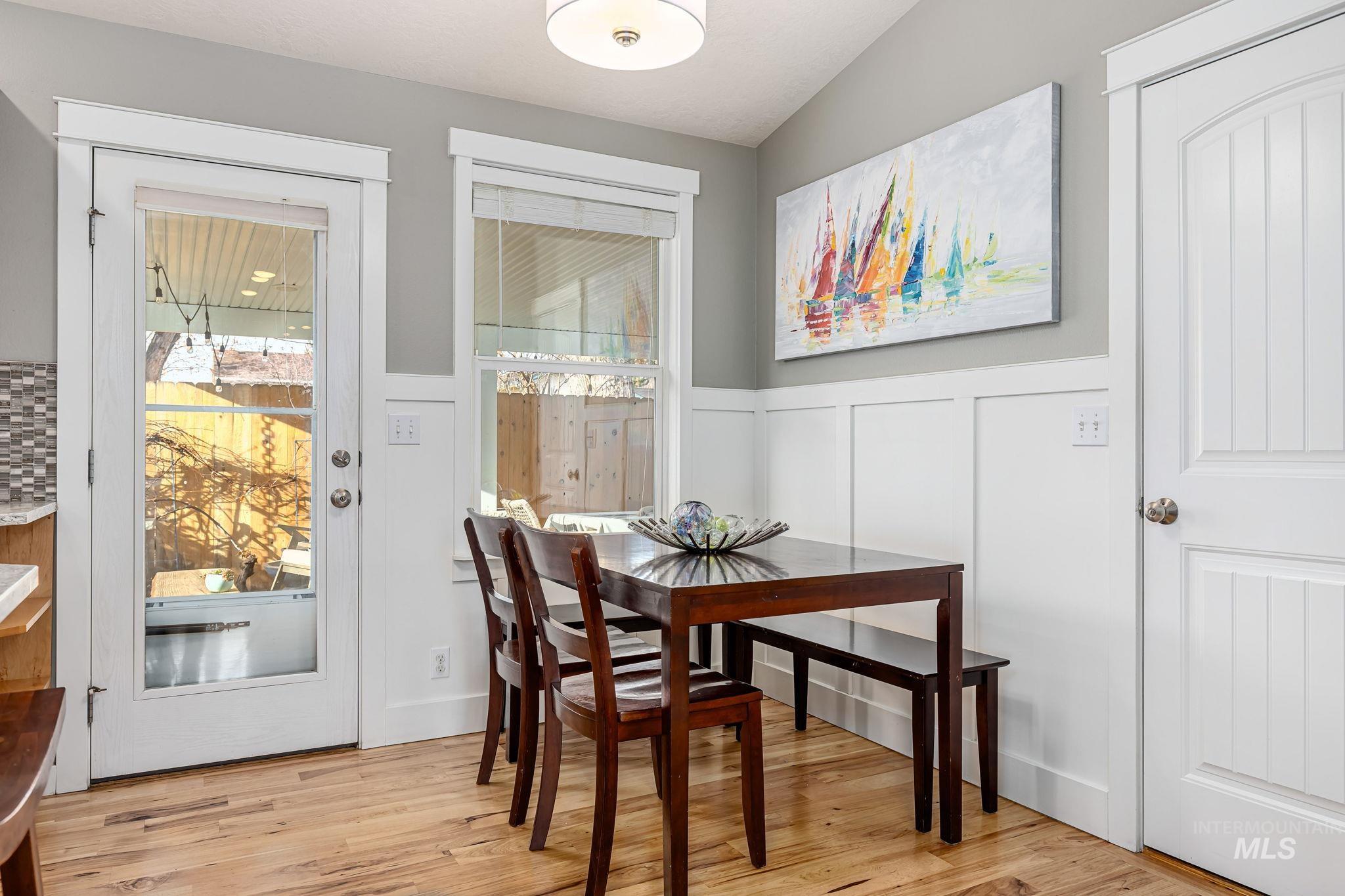 Dining area with a wainscoted wall, light wood finished floors, a decorative wall, and vaulted ceiling