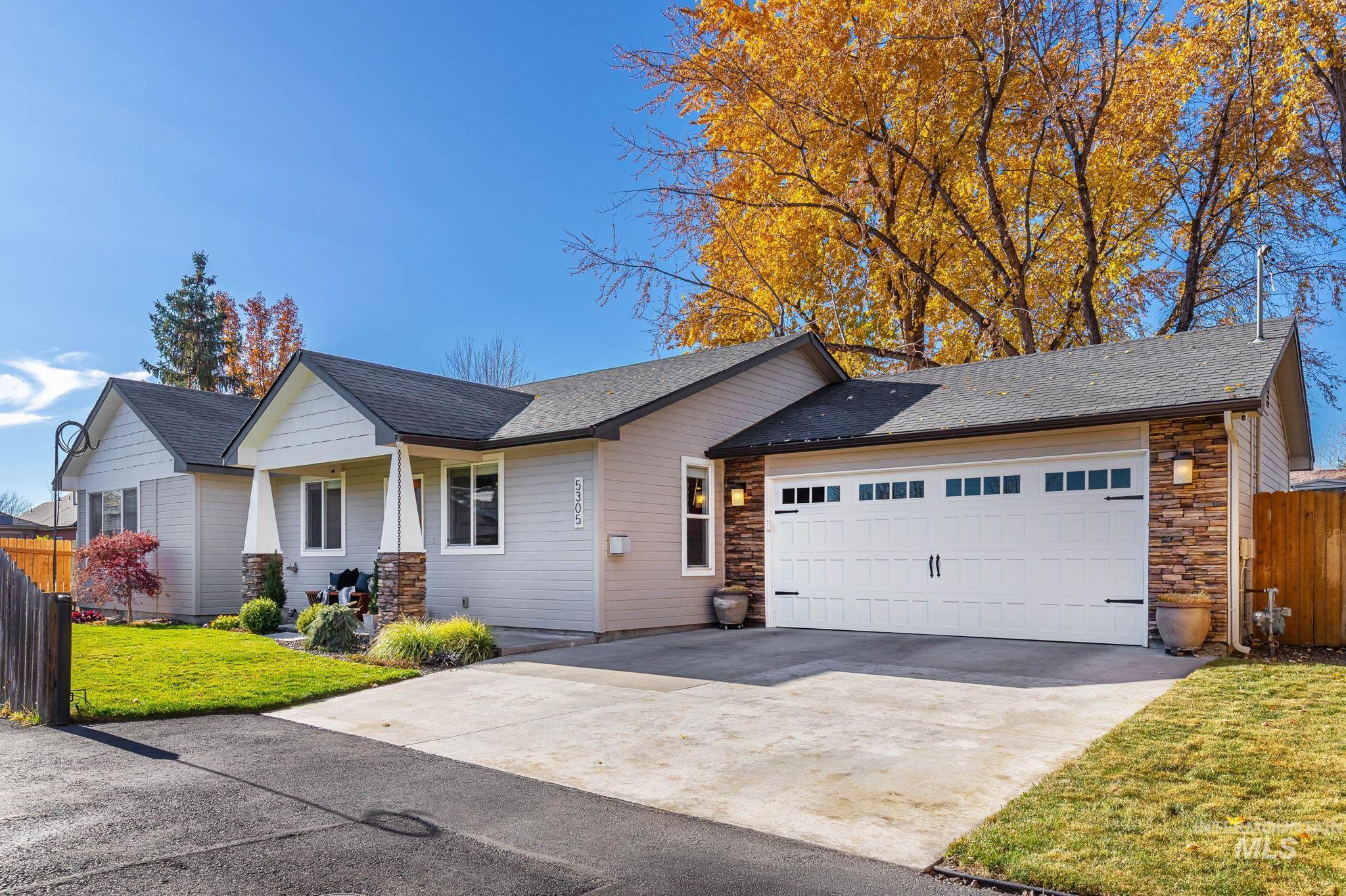 View of front of house with a shingled roof, driveway, an attached garage, stone siding, and covered porch