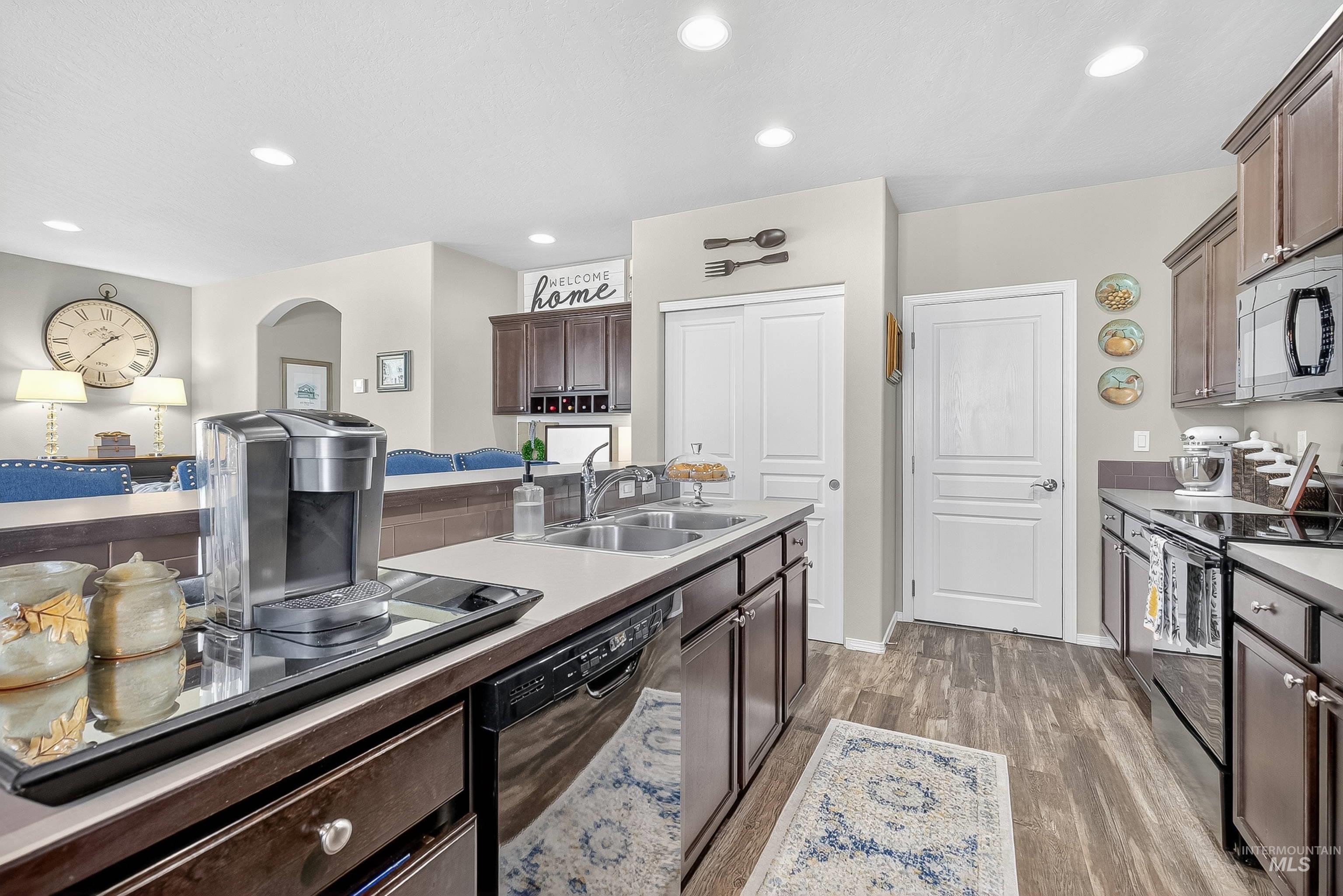Kitchen with dark brown cabinets, black appliances, recessed lighting, and light wood-style flooring