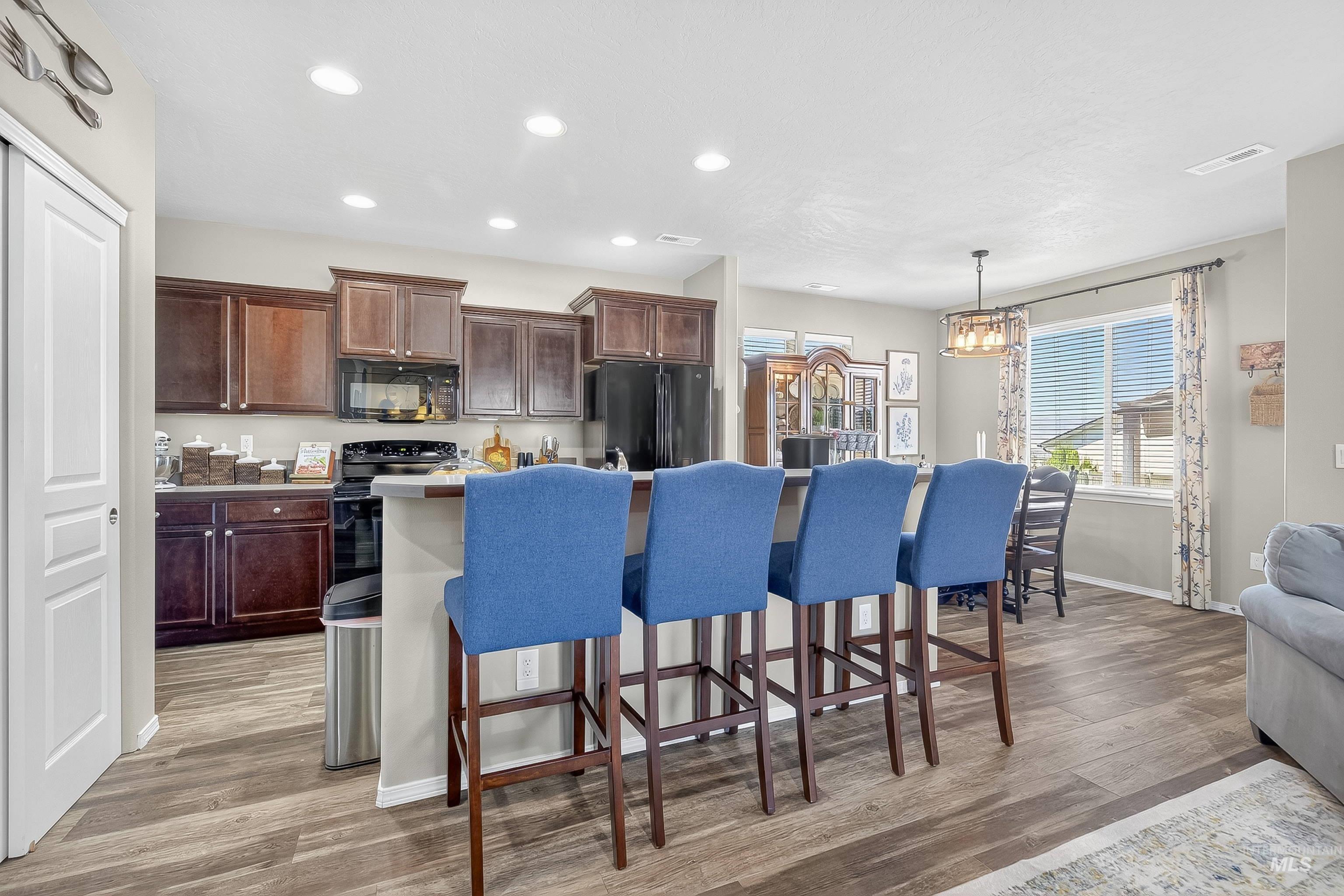 Kitchen with a kitchen breakfast bar, recessed lighting, a kitchen island with sink, dark brown cabinetry, and light wood-type flooring