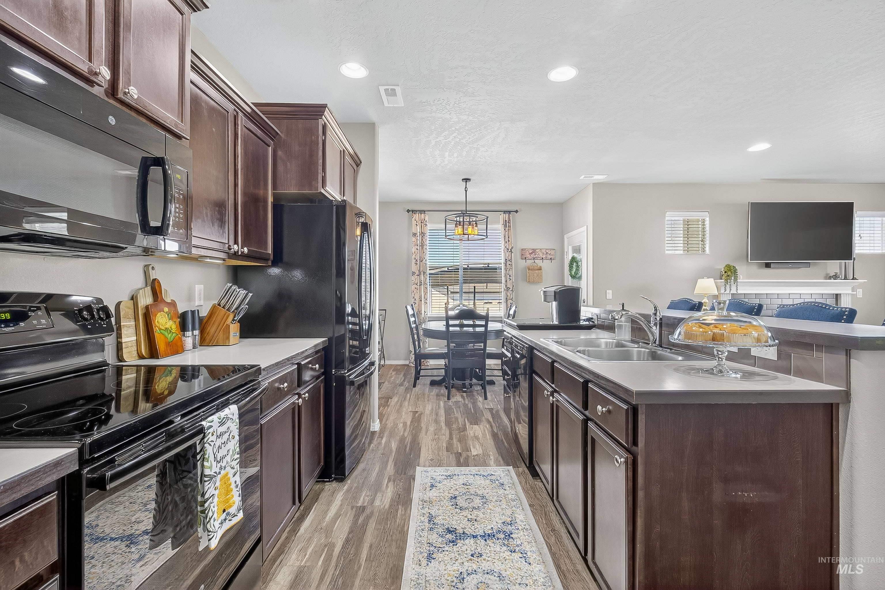 Kitchen with black appliances, dark brown cabinets, an island with sink, light wood-style floors, and recessed lighting