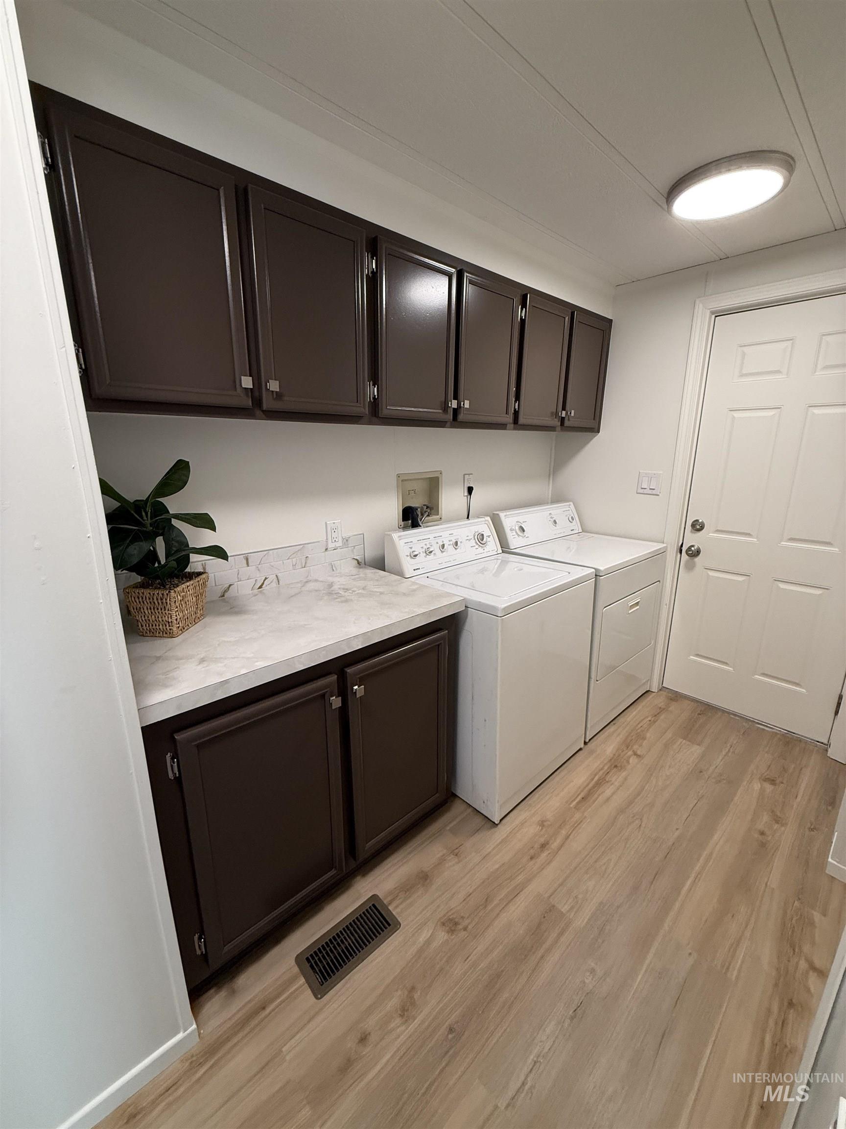 Laundry room with light wood finished floors, washing machine and dryer, and cabinet space