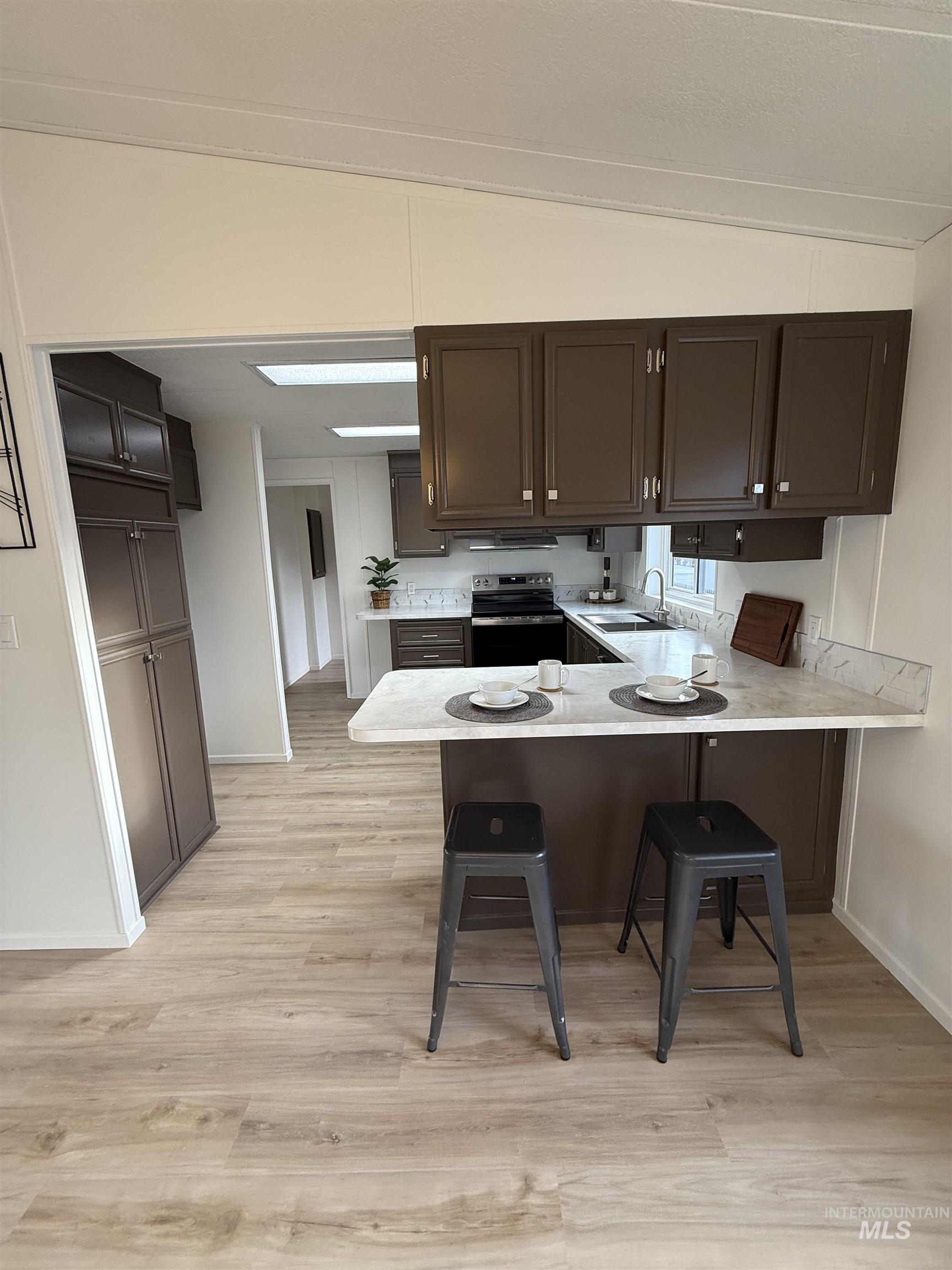 Kitchen featuring a kitchen breakfast bar, a peninsula, light countertops, stainless steel range with electric cooktop, and light wood-style floors