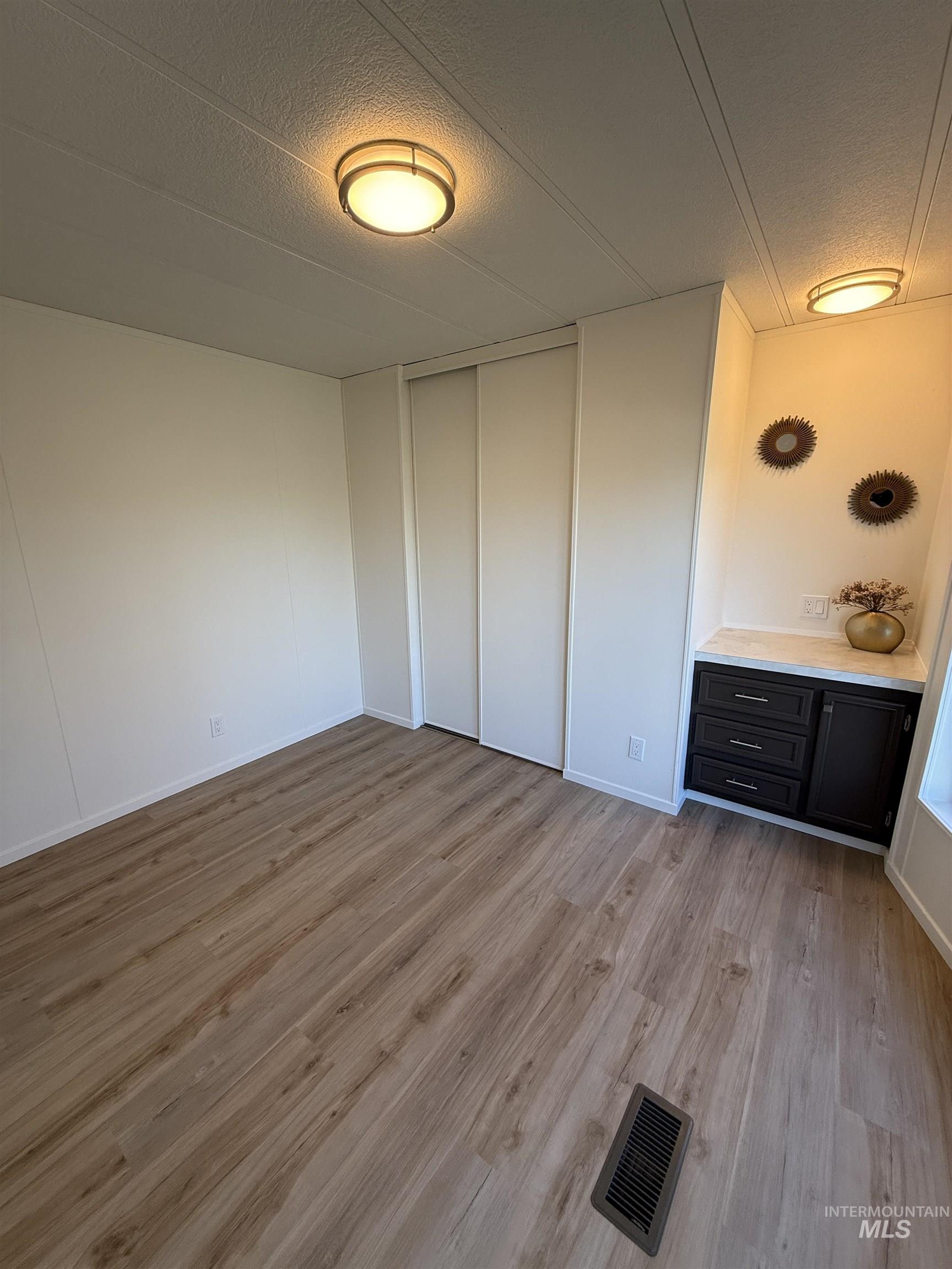 Unfurnished bedroom featuring light wood finished floors, a textured ceiling, and a closet